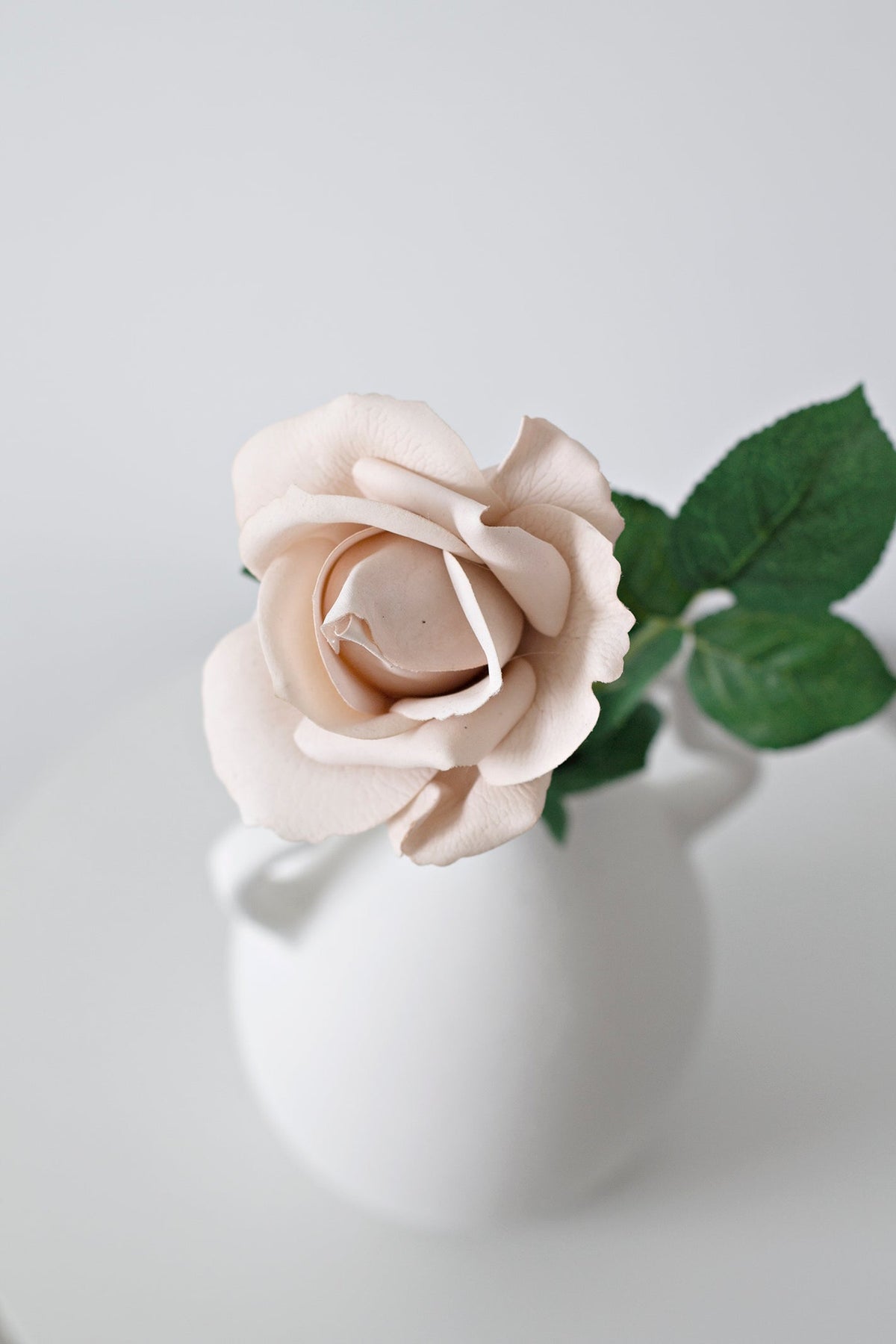 Close view of a light brown tea rose in a white handled vase