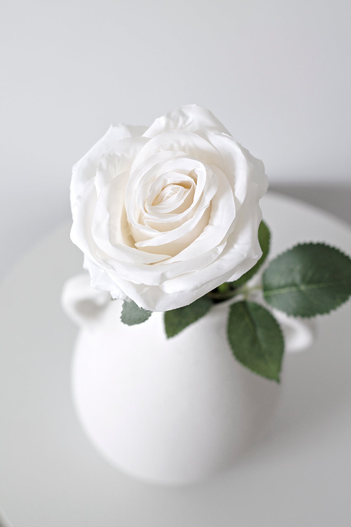 Close view of a white faux rose in a handled white vase