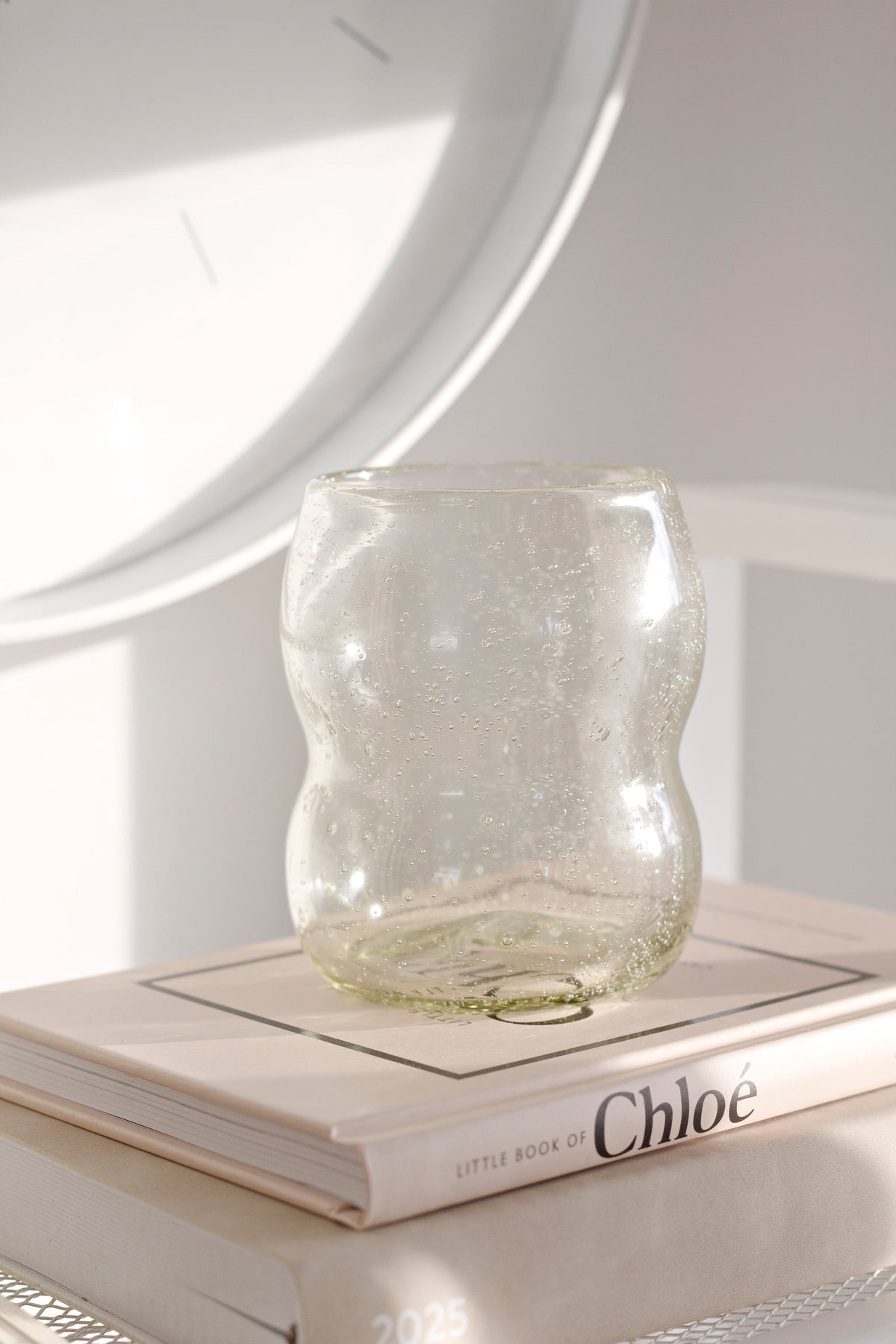 Light amber tumbler on a coffee table book below a round mirror