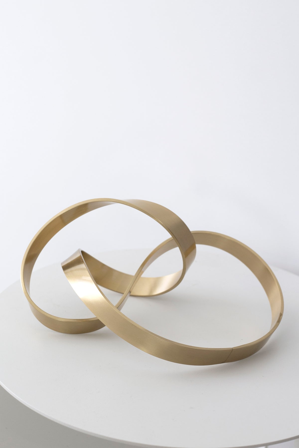 Gold Infinity Loop sculpture on a round white side table