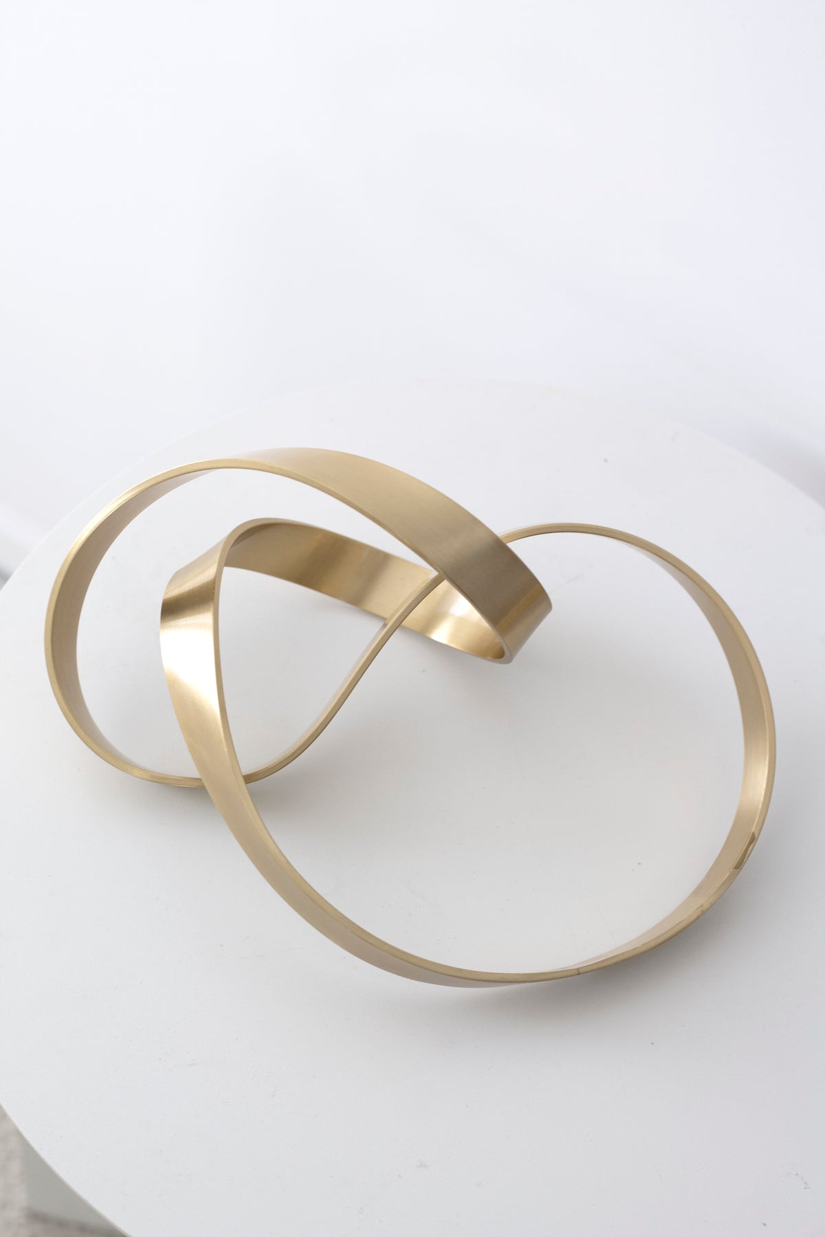 Gold Infinity Loop sculpture photographed from above on a white surface