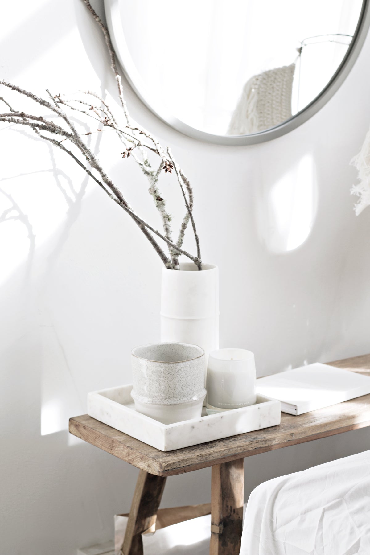 Umbra Hub round mirror in grey above a rustic bench with ceramics and branches