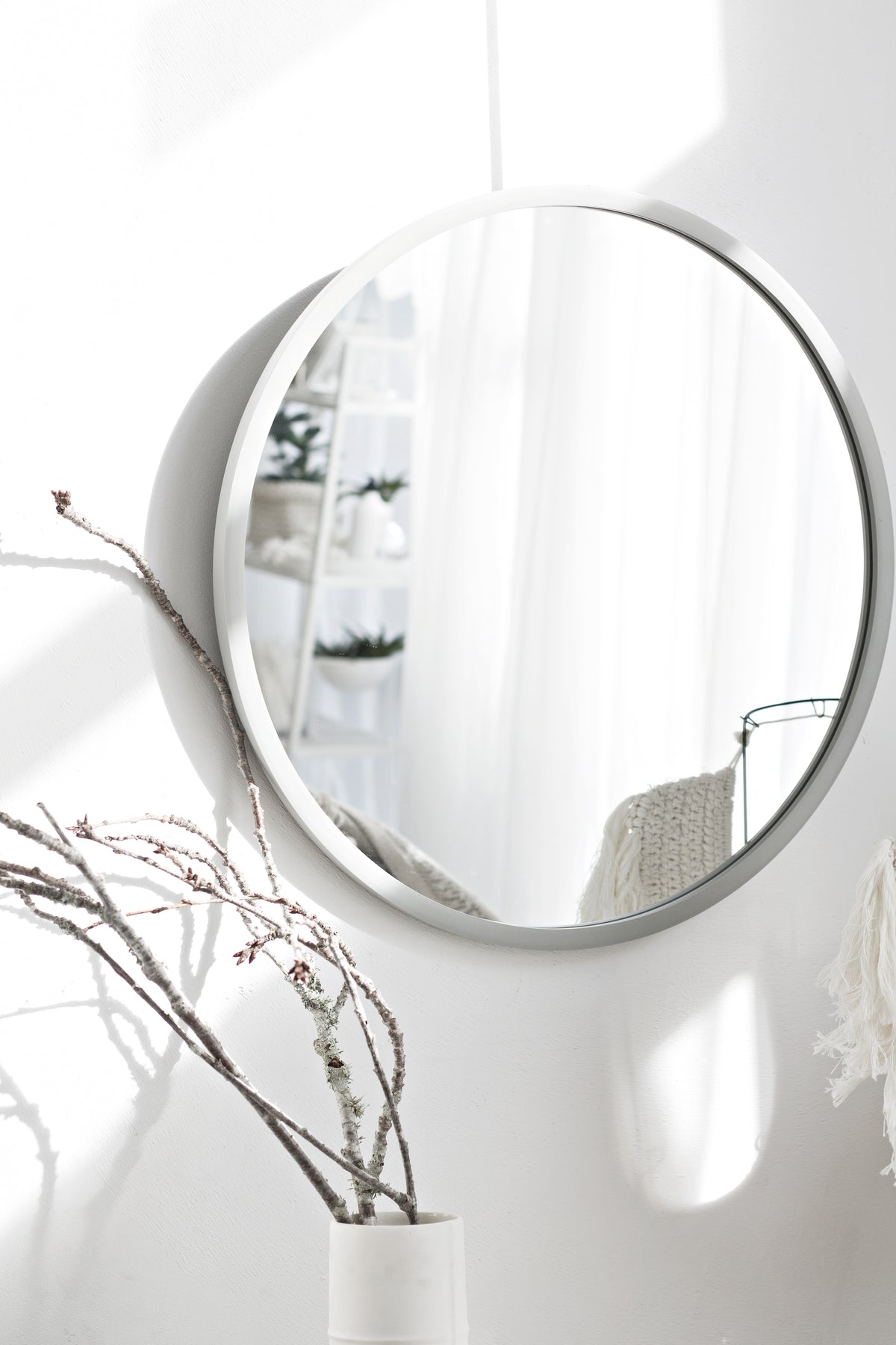 Umbra Hub round mirror in grey on a white wall reflecting a bright room