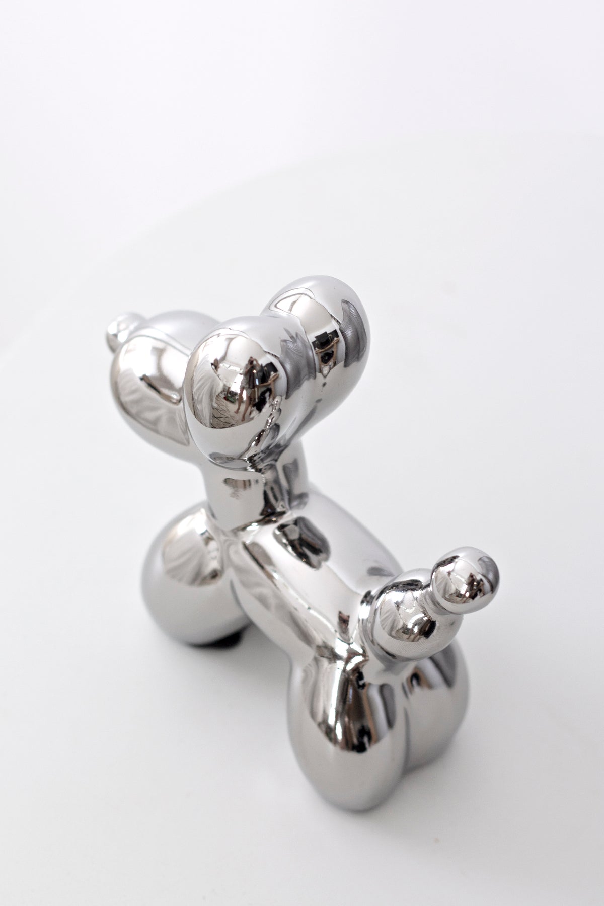 Silver ceramic balloon dog sculpture on a white surface, angled view