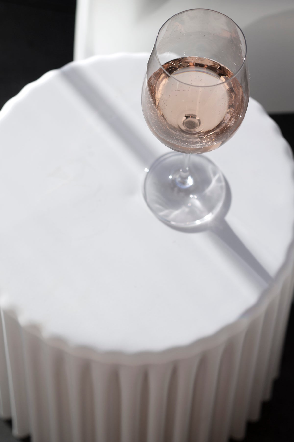 Looking down on a nude ribbed stool top with a glass of rose wine and a stripe of sunlight
