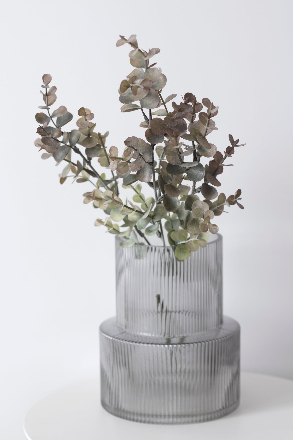 Faux eucalyptus stems in a stone-look vase on a pale surface