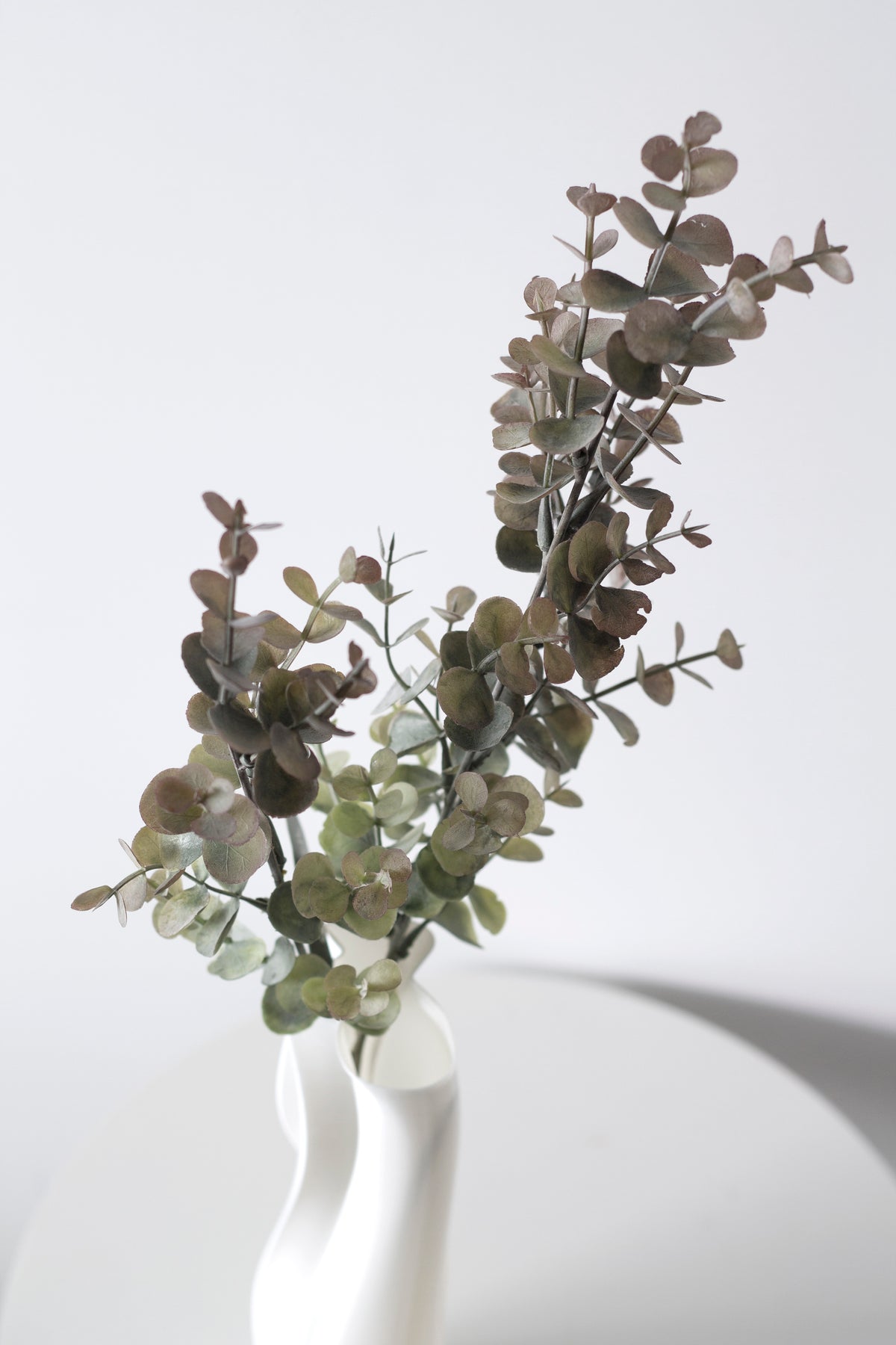Faux eucalyptus stems with mauve tones in a white vase