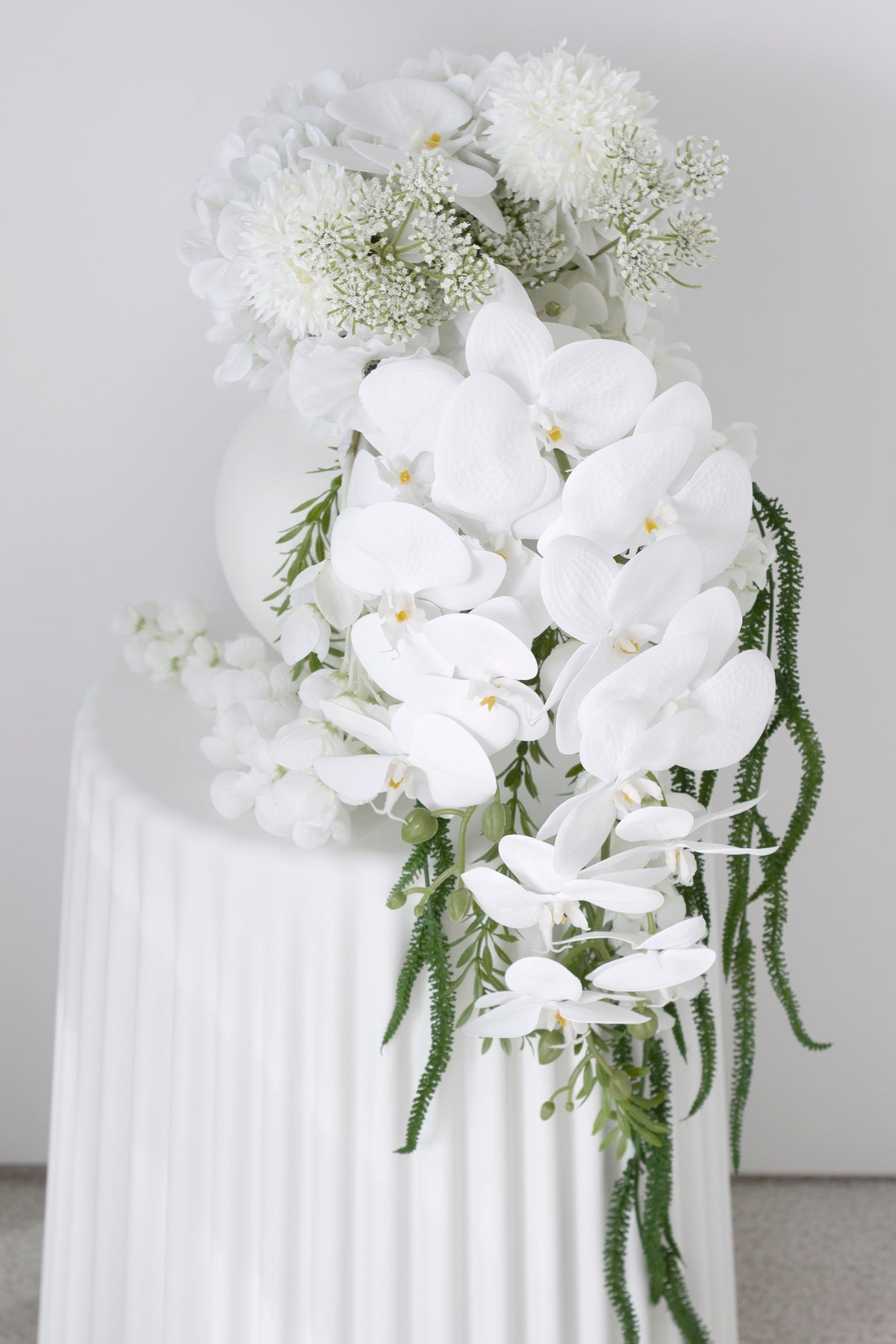 Orchids and hydrangeas in a ribbed cylinder vase, greenery spilling low at the front