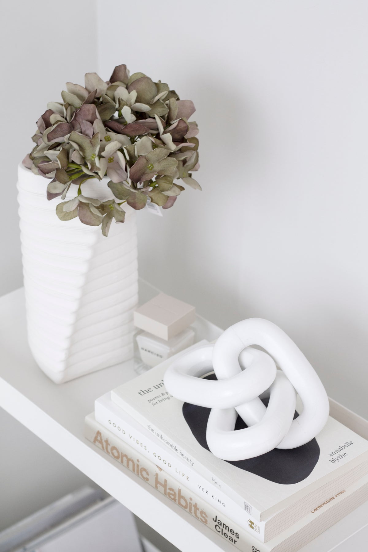 White wooden chain in a black dish on books, with a ribbed white vase of dried hydrangea behind