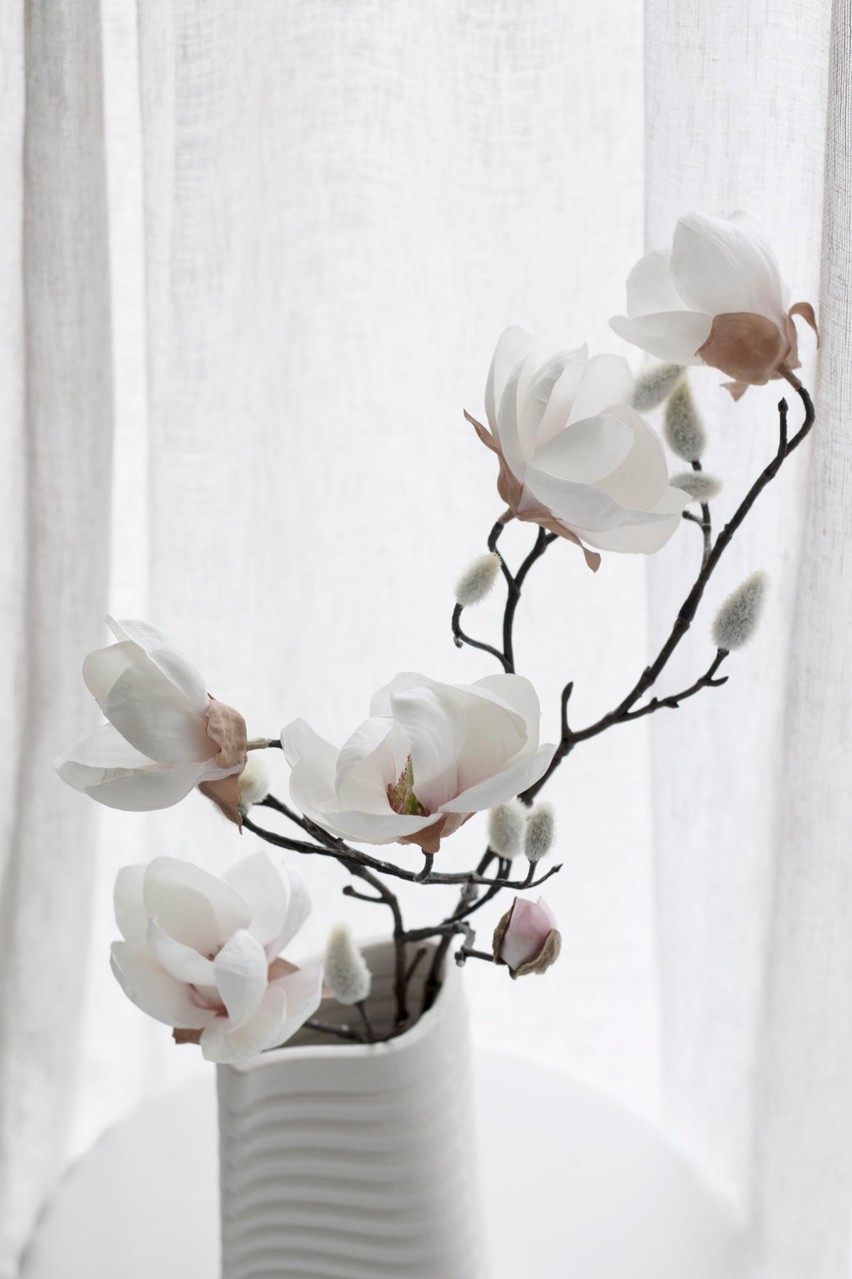 Close view of white faux magnolia blooms with dark branches in a white vase