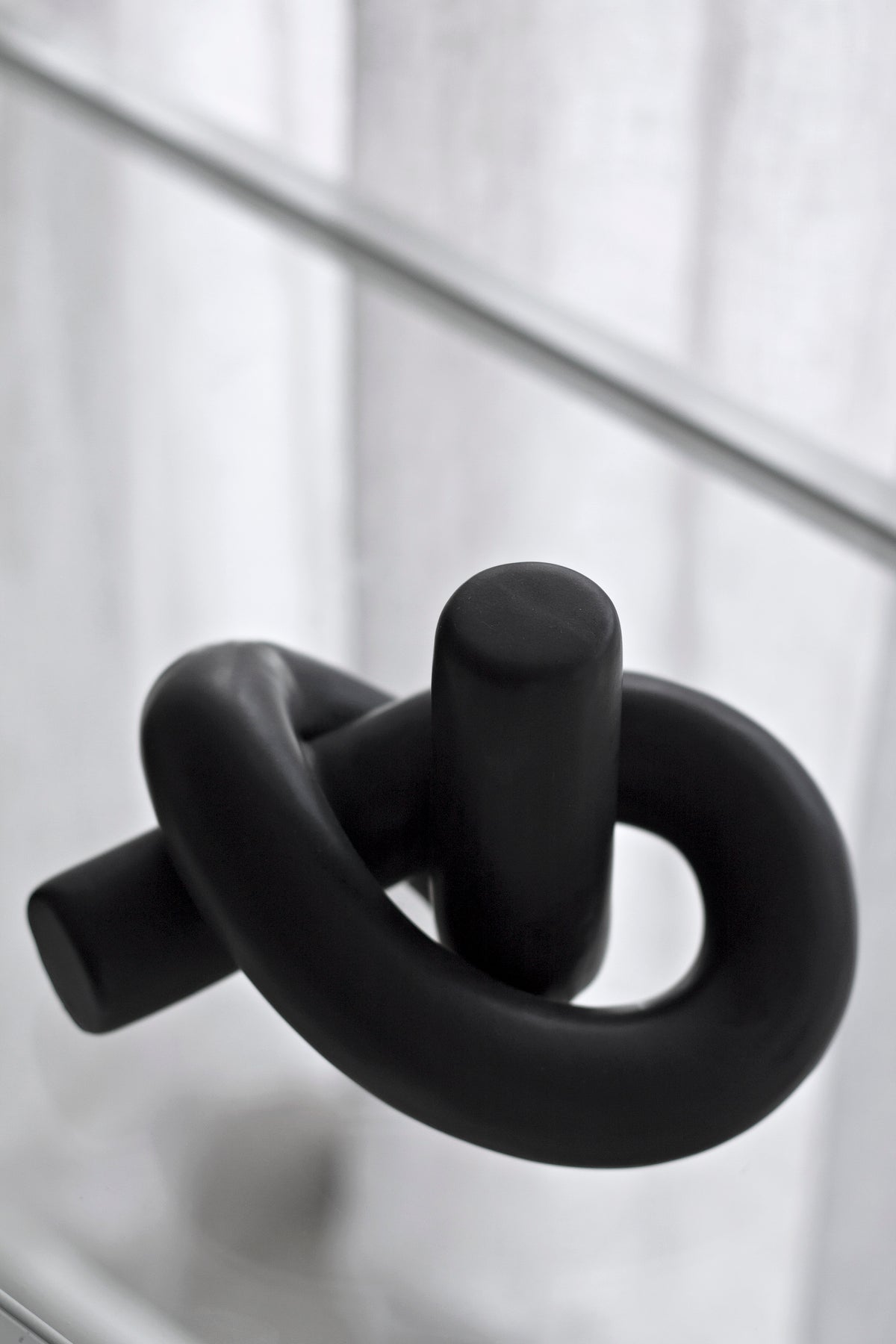 Black Knot Ornament close up on a pale ledge, showing the rounded matte tube form