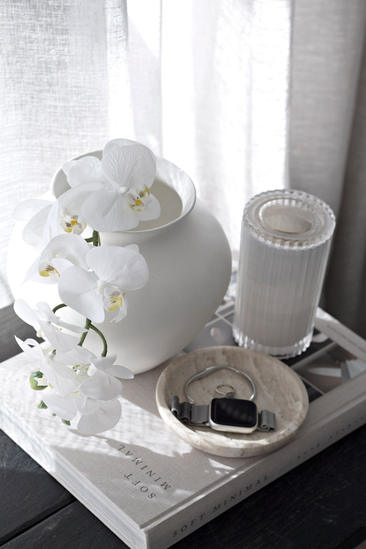 Tray holding dark trinkets next to a white orchid vase and a ribbed candle