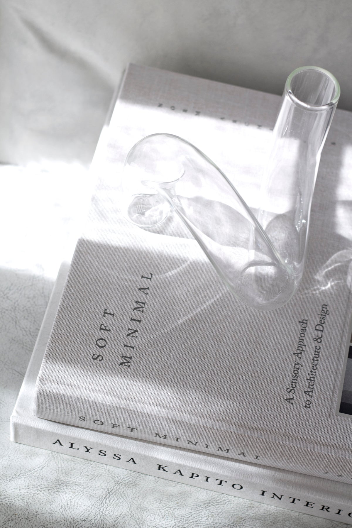 Clear J-Curve vase on a stack of books in strong sunlight, shadows across the covers