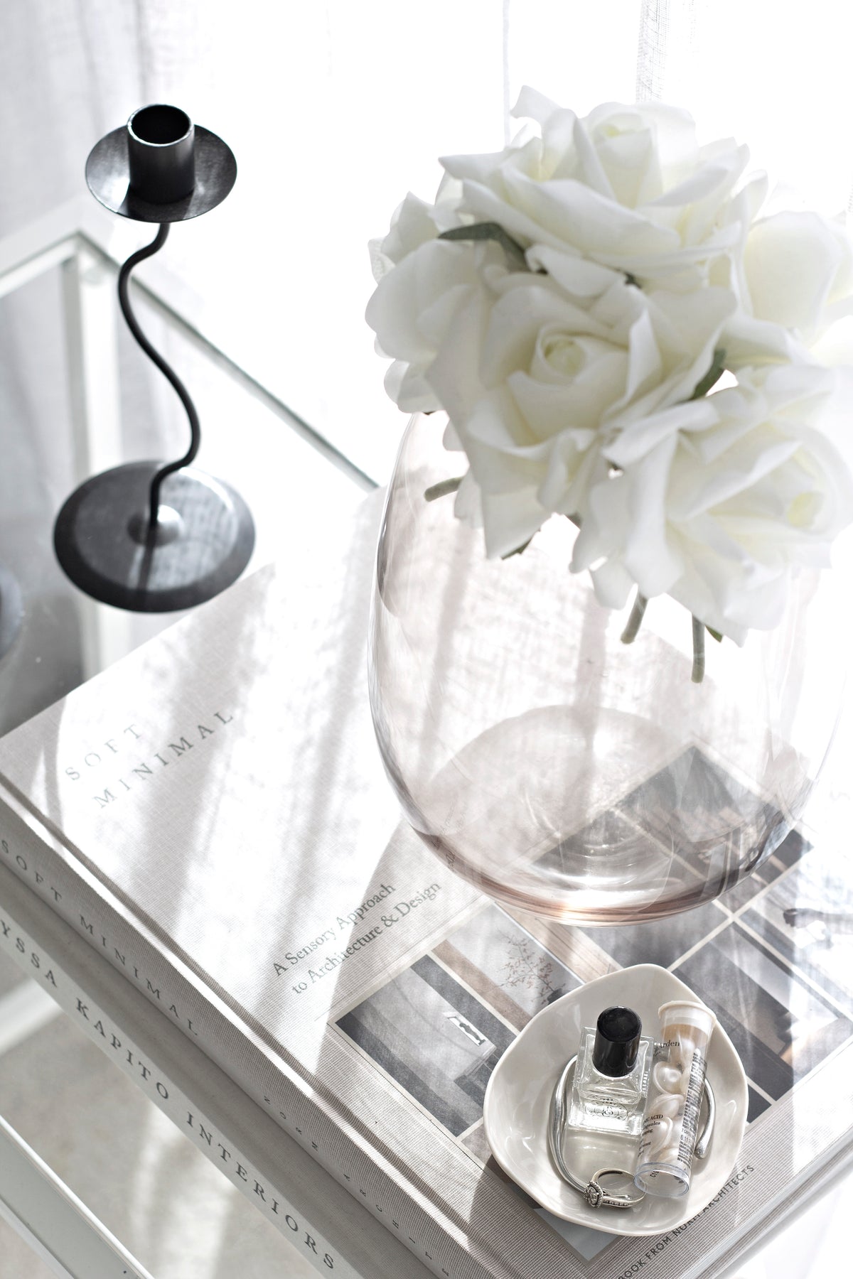 Black Hera holder on a mirrored tray with white roses in a glass vase and a fragrance bottle