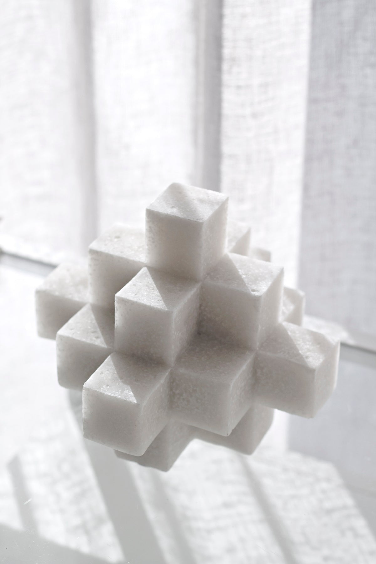 White Cubism sculpture in front of a sunlit sheer curtain