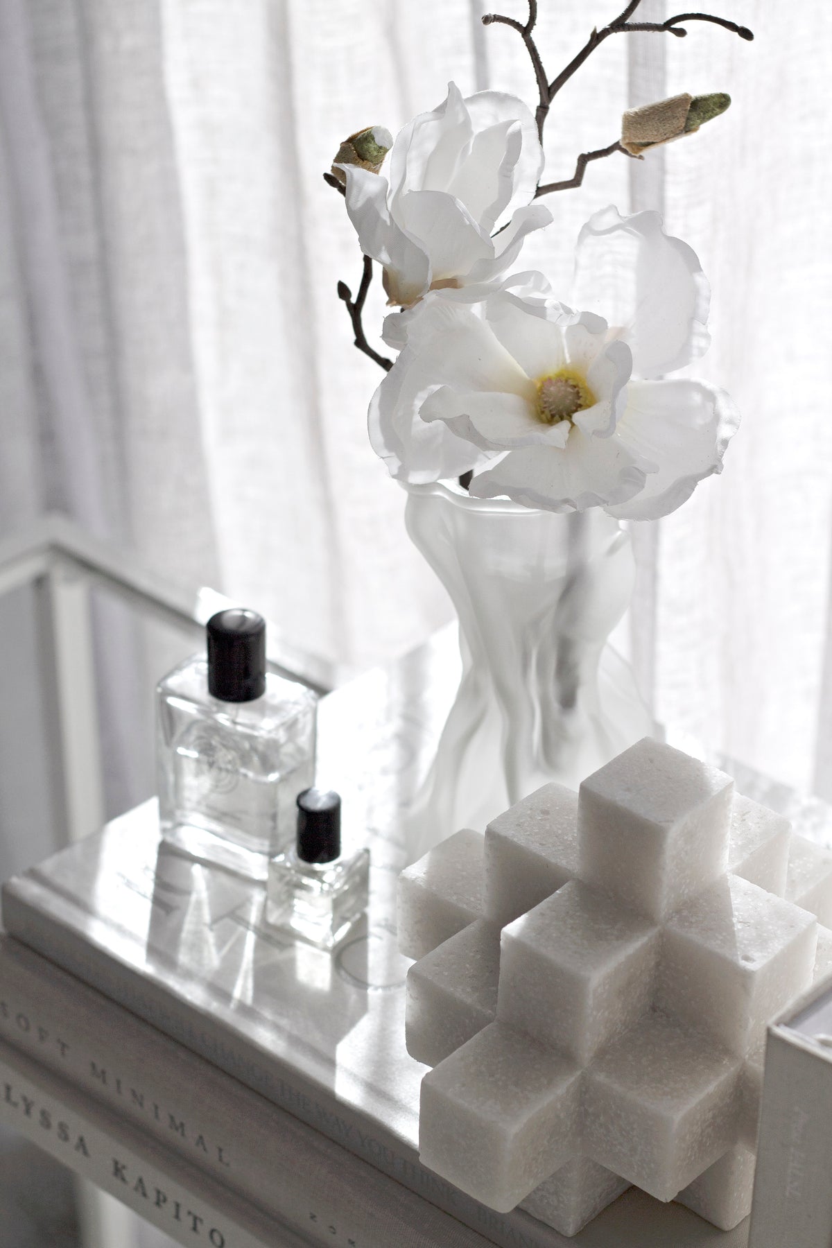 White Cubism sculpture on a windowsill with a perfume bottle and white flowers