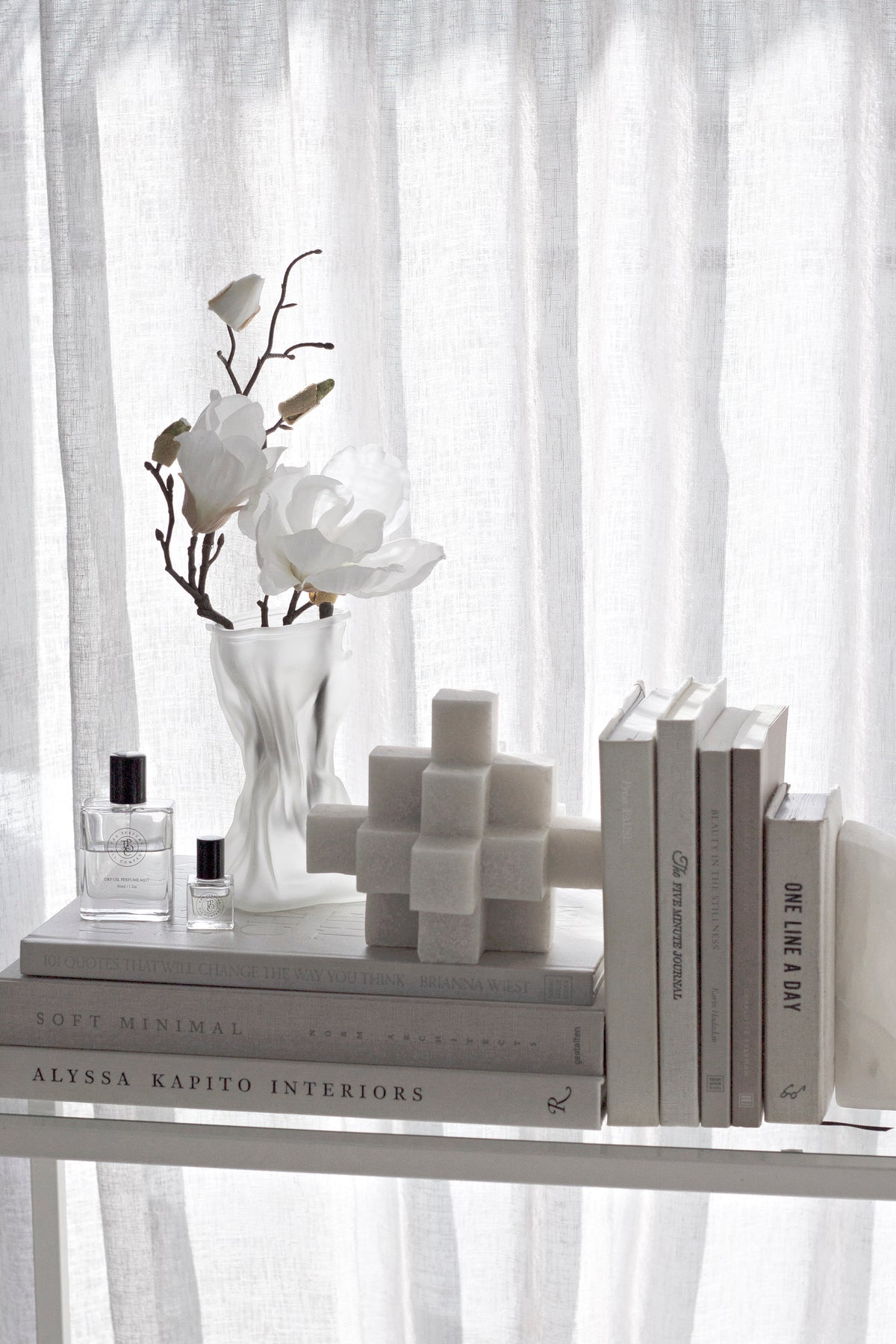 White Cubism sculpture on books on a shelf with white flowers behind