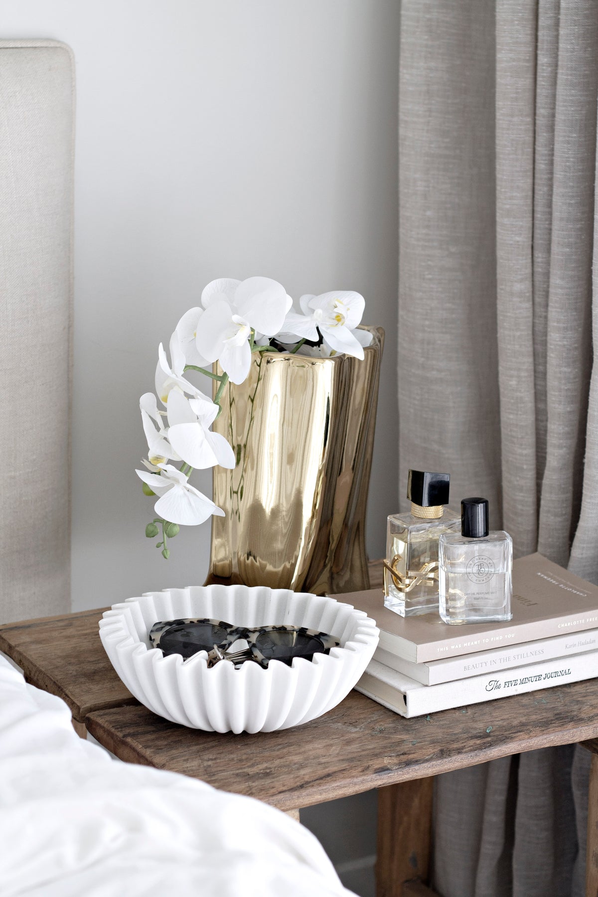 Gold metallic bag vase with a white orchid on a timber bedside table with a fluted bowl
