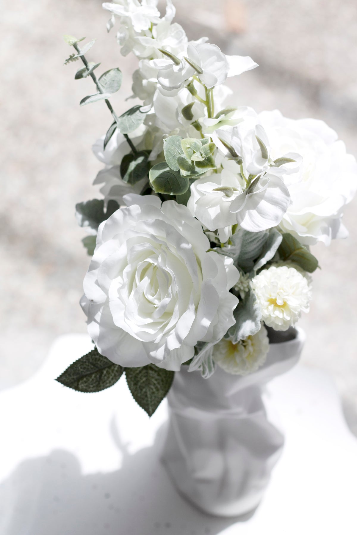 White faux bouquet in a sculptural face vase on a white surface