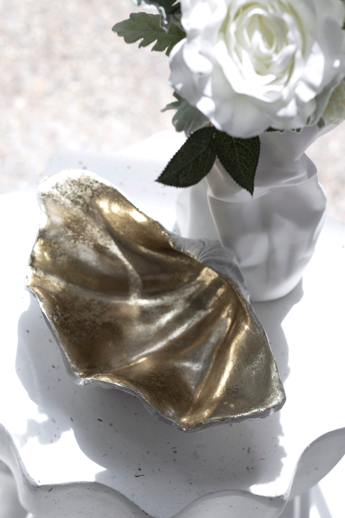 Upright champagne clam shell in front of a vase of white roses