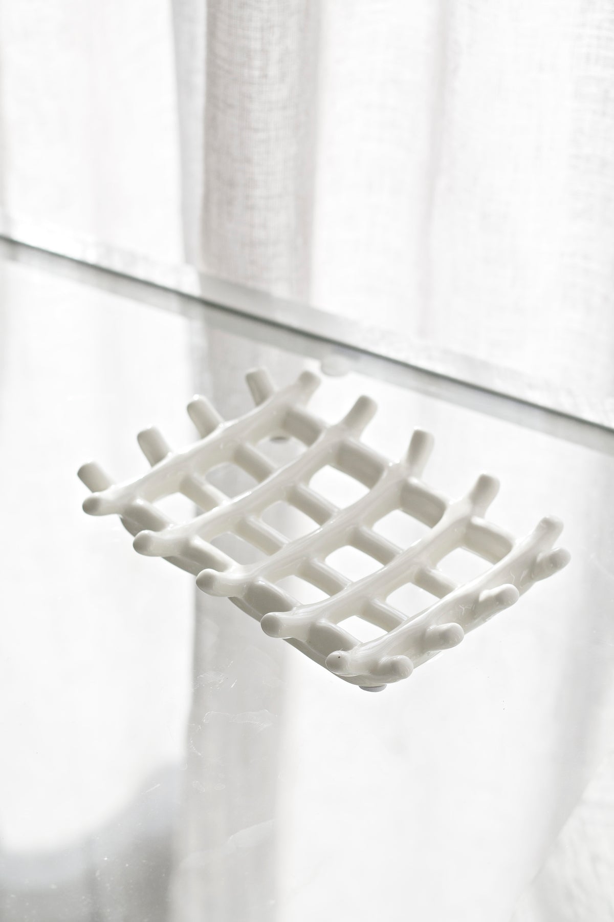Soap dish on a glass shelf with a sheer curtain filtering daylight behind