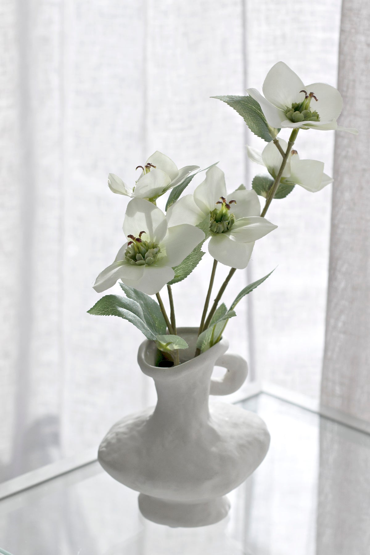 Cream hellebores in a grey vase with small handles by a window