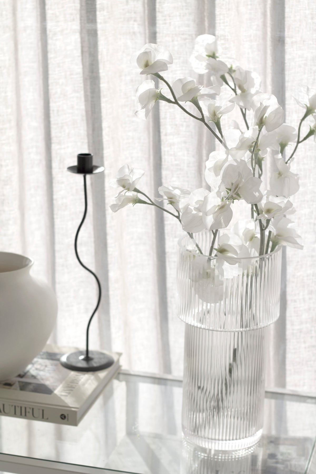 Sweet peas in a ribbed glass vase beside a wavy candle holder on books