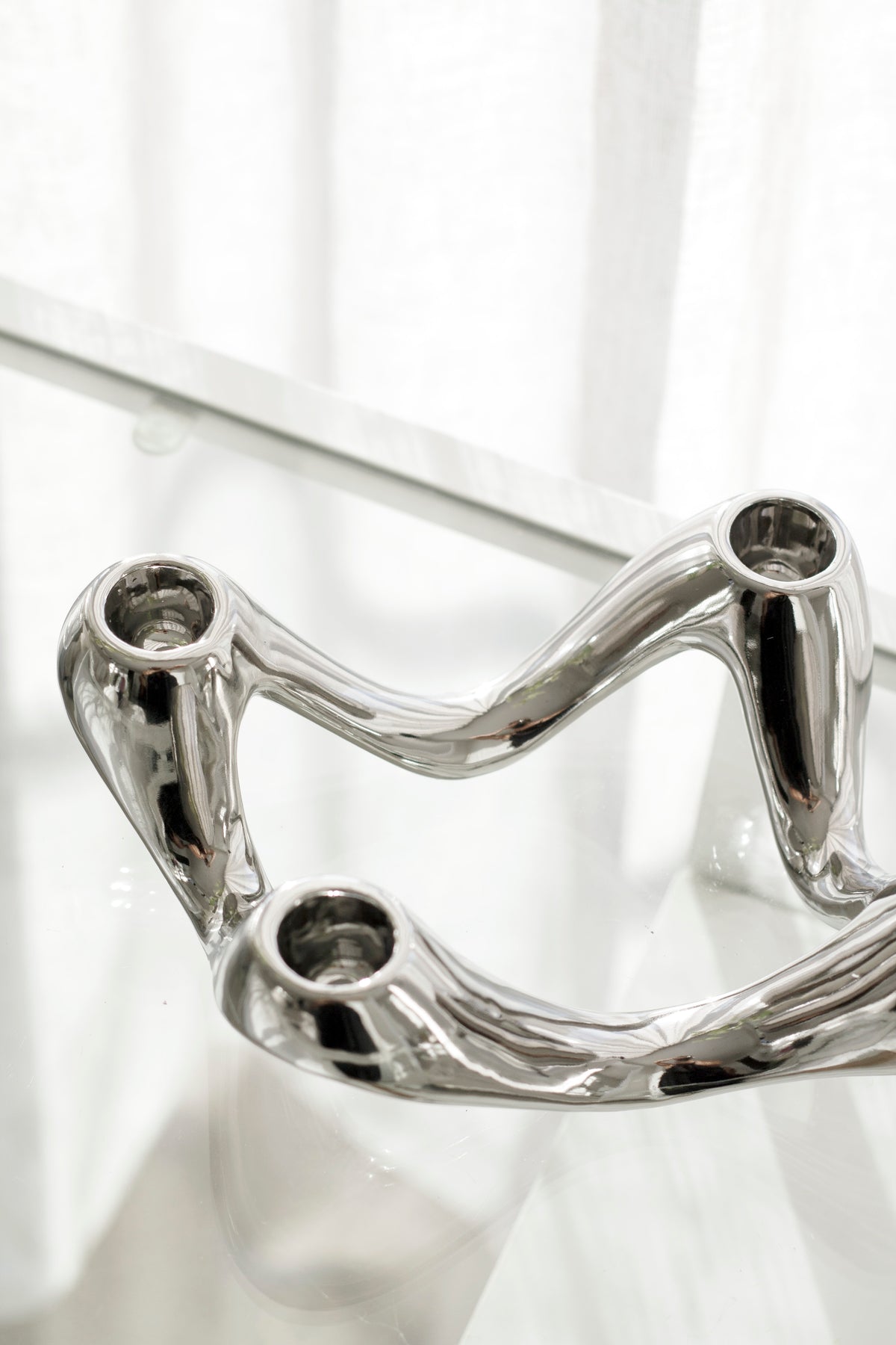 Close on the silver candle holder against a sheer curtain, sockets catching the light