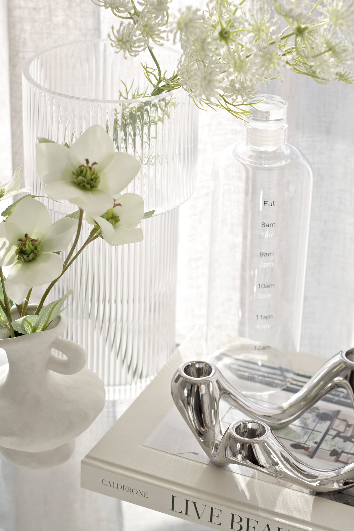 Silver candle holder on a book beside a ribbed vase and a slim glass bottle