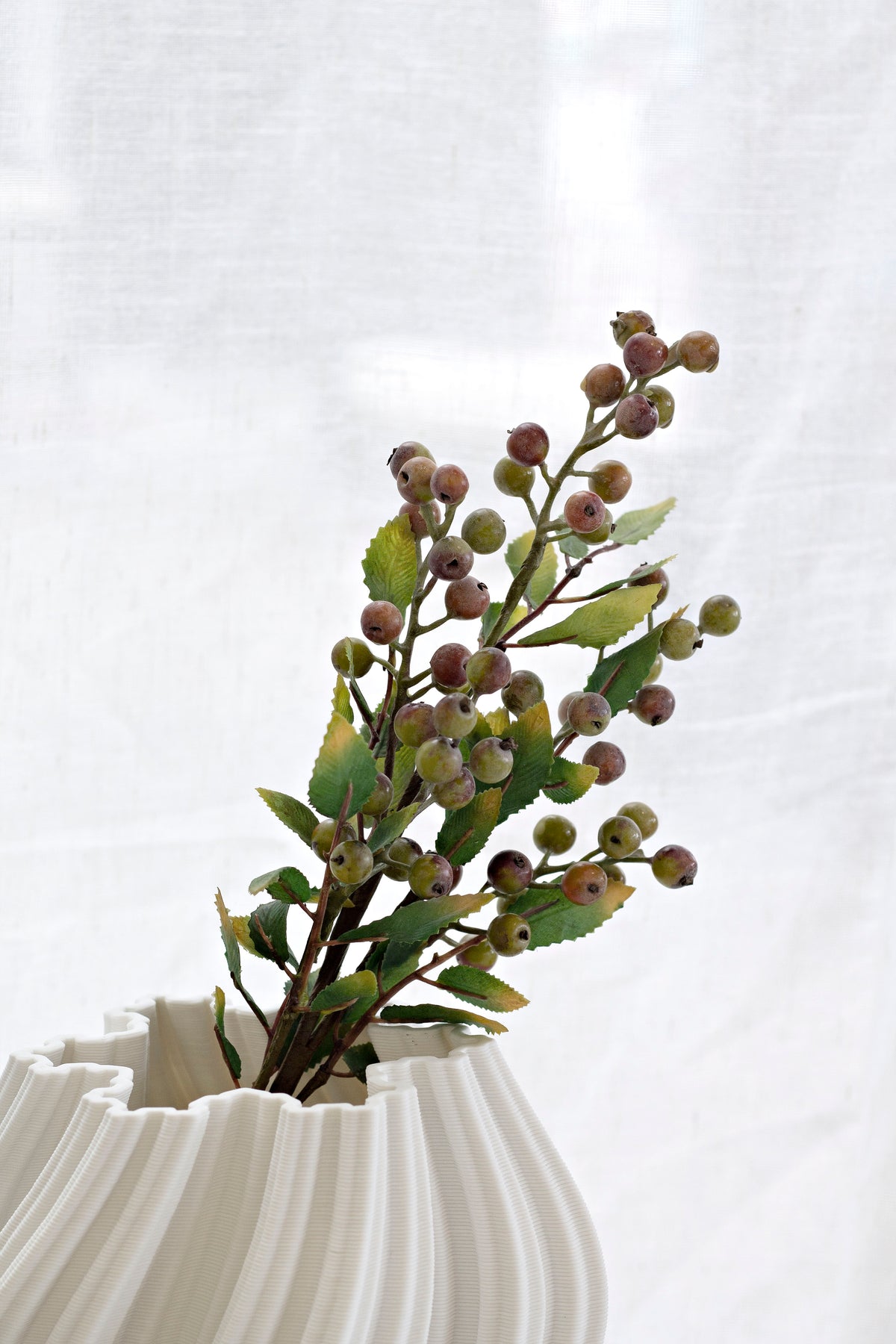 Summer berry branch styled in a white fluted vase against a sheer curtain
