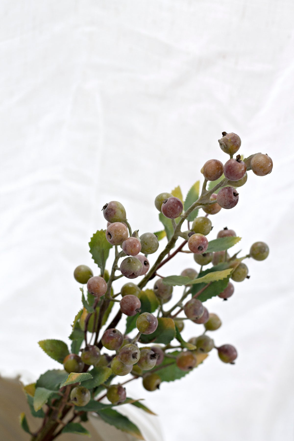 Faux summer berry branch angled against soft white linen, showing berries and foliage