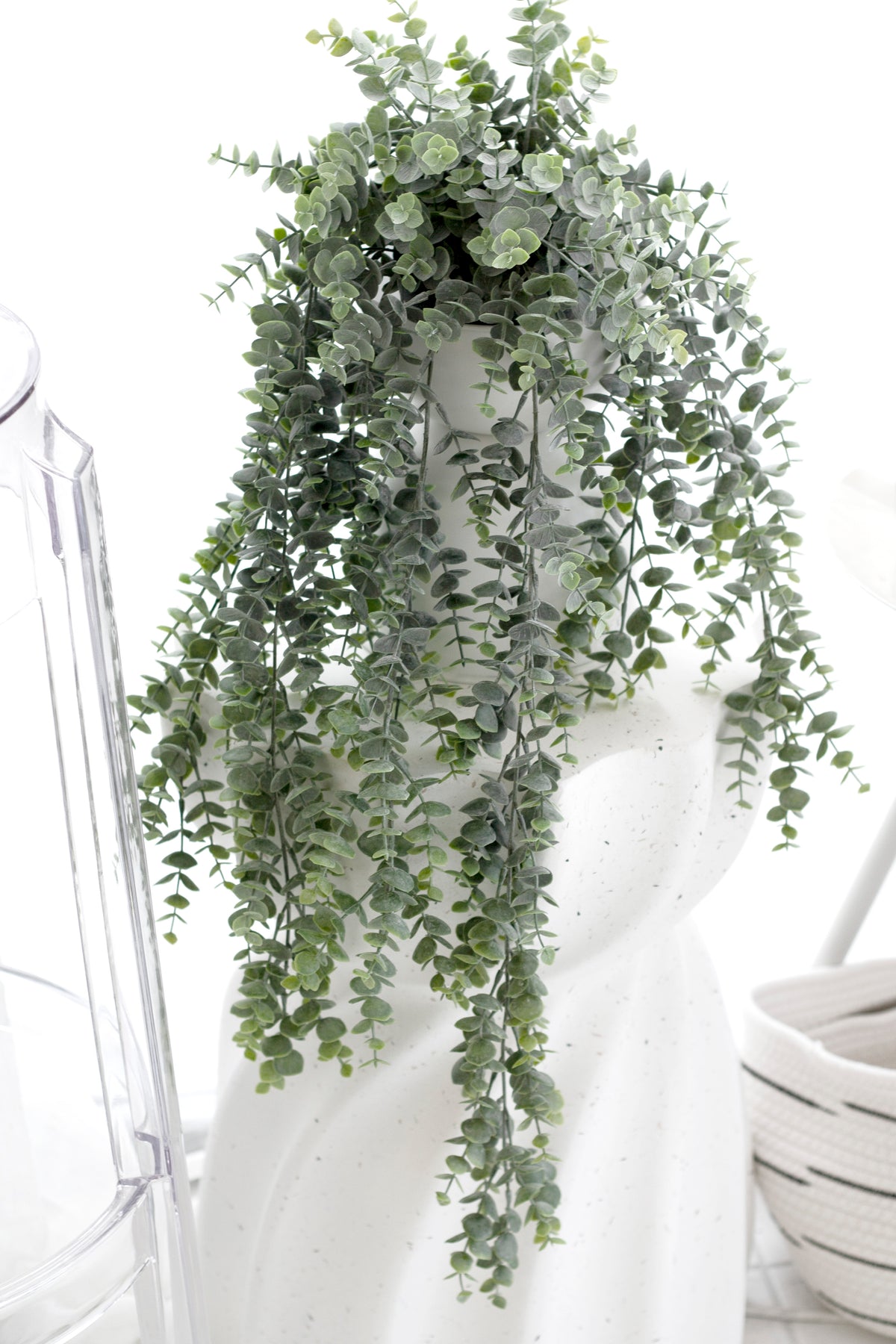 Grey-green eucalyptus in a textured white pot on a bathroom shelf beside folded towels