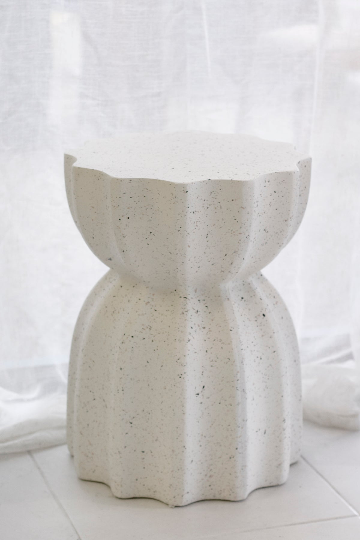 Fleck white fluted side table beside a linen curtain, speckles across the surface
