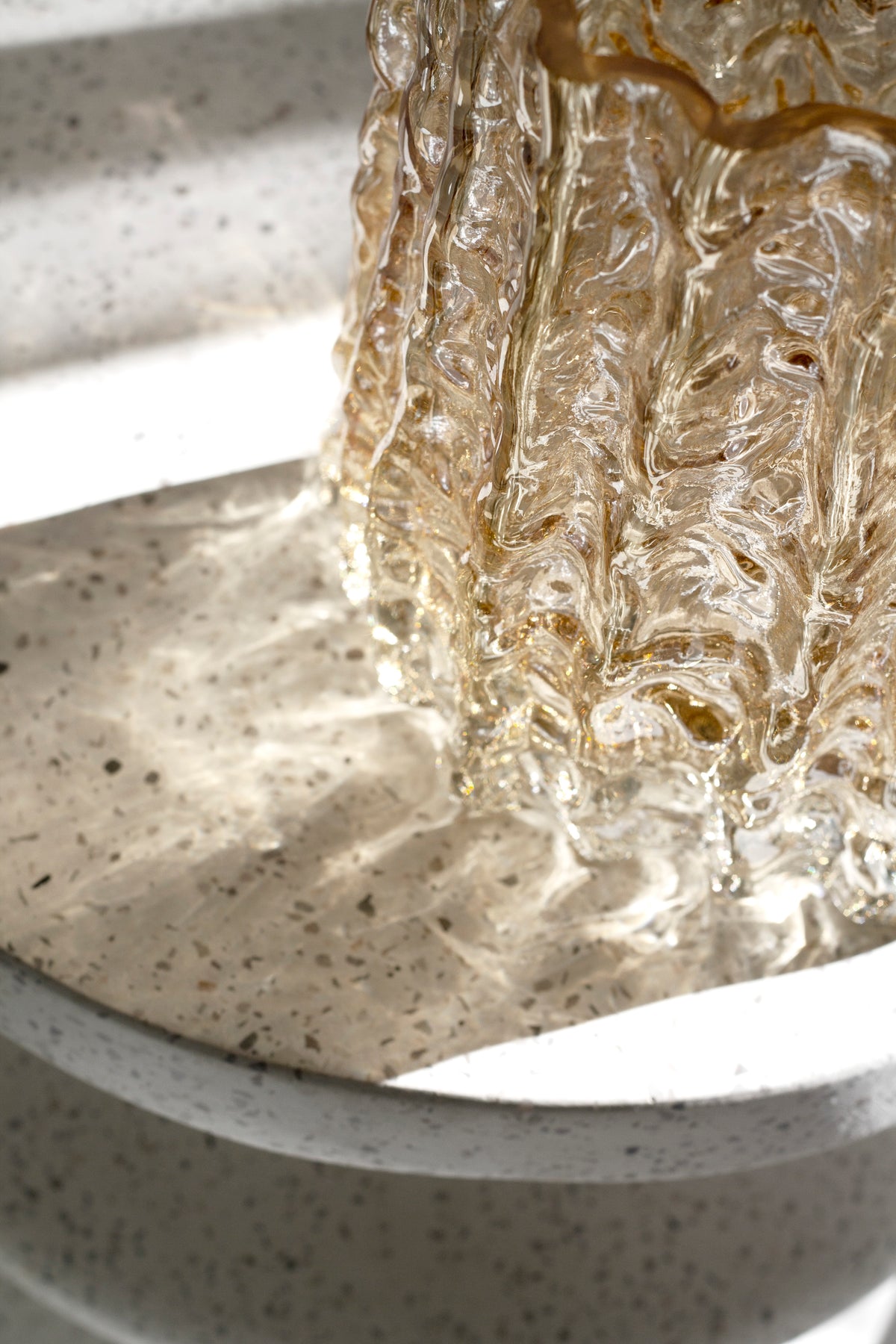 Close up of the gold Glacier vase base resting on a speckled stone pedestal