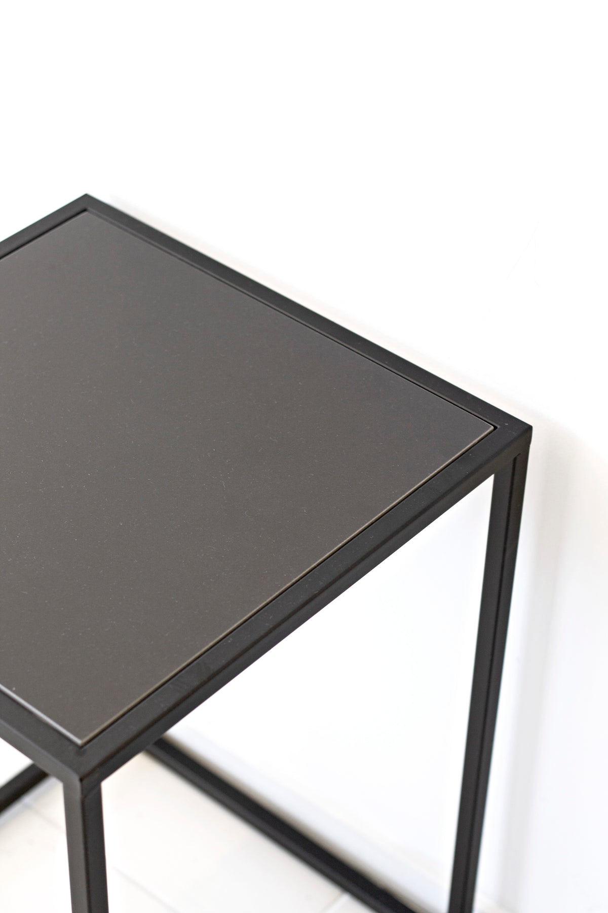 Close view of the Sara table's corner, where the dark top panel meets the welded black frame