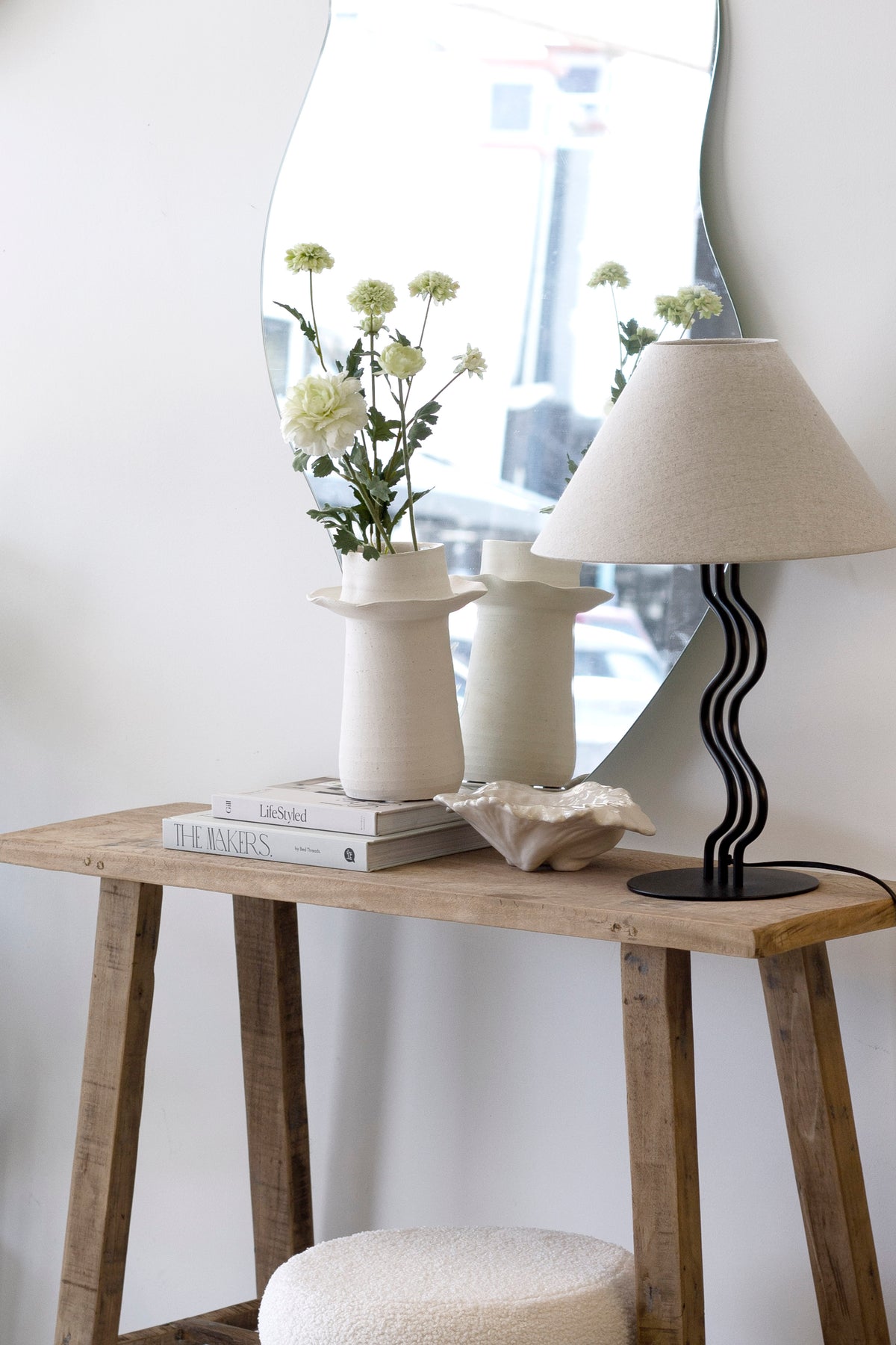 Recycled teak console styled with a cream lamp, vases of daisies and books beside a mirror