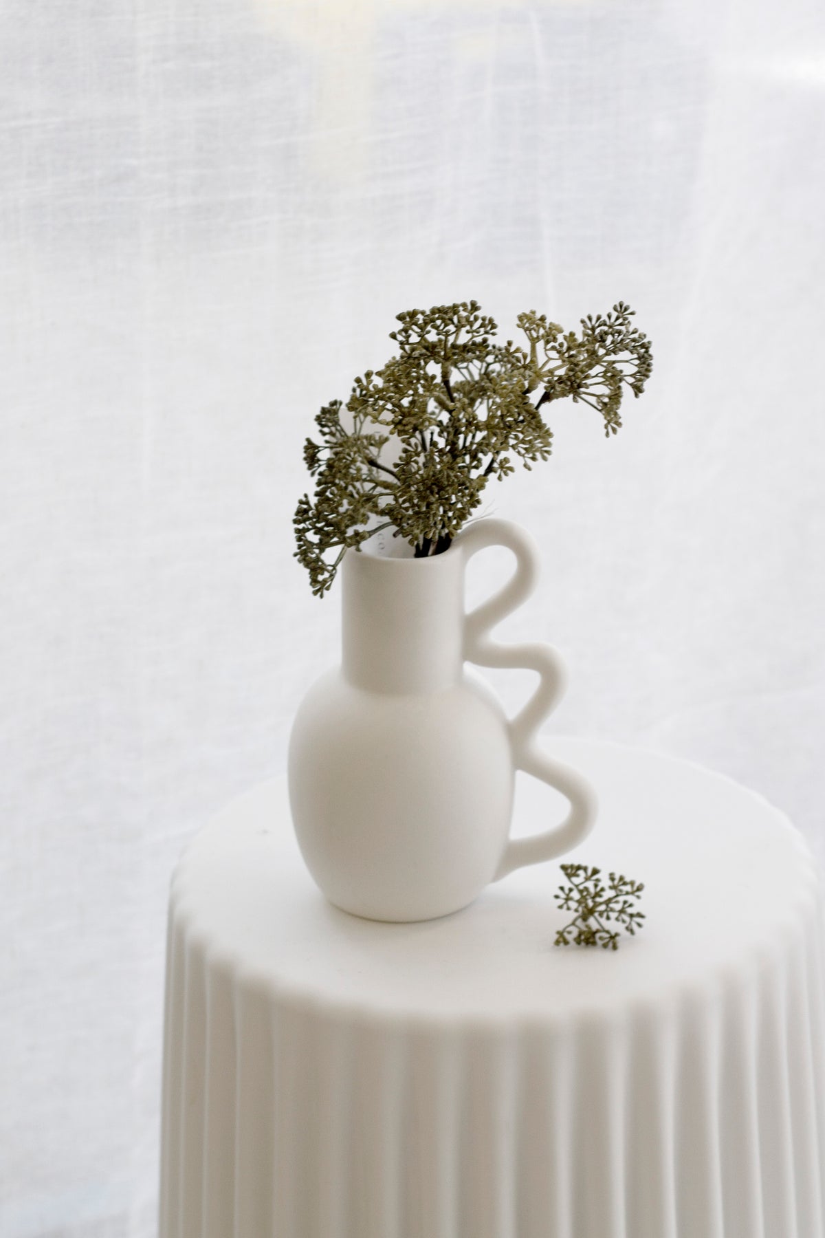 Chloe vase of green blossom stems on a fluted white pedestal