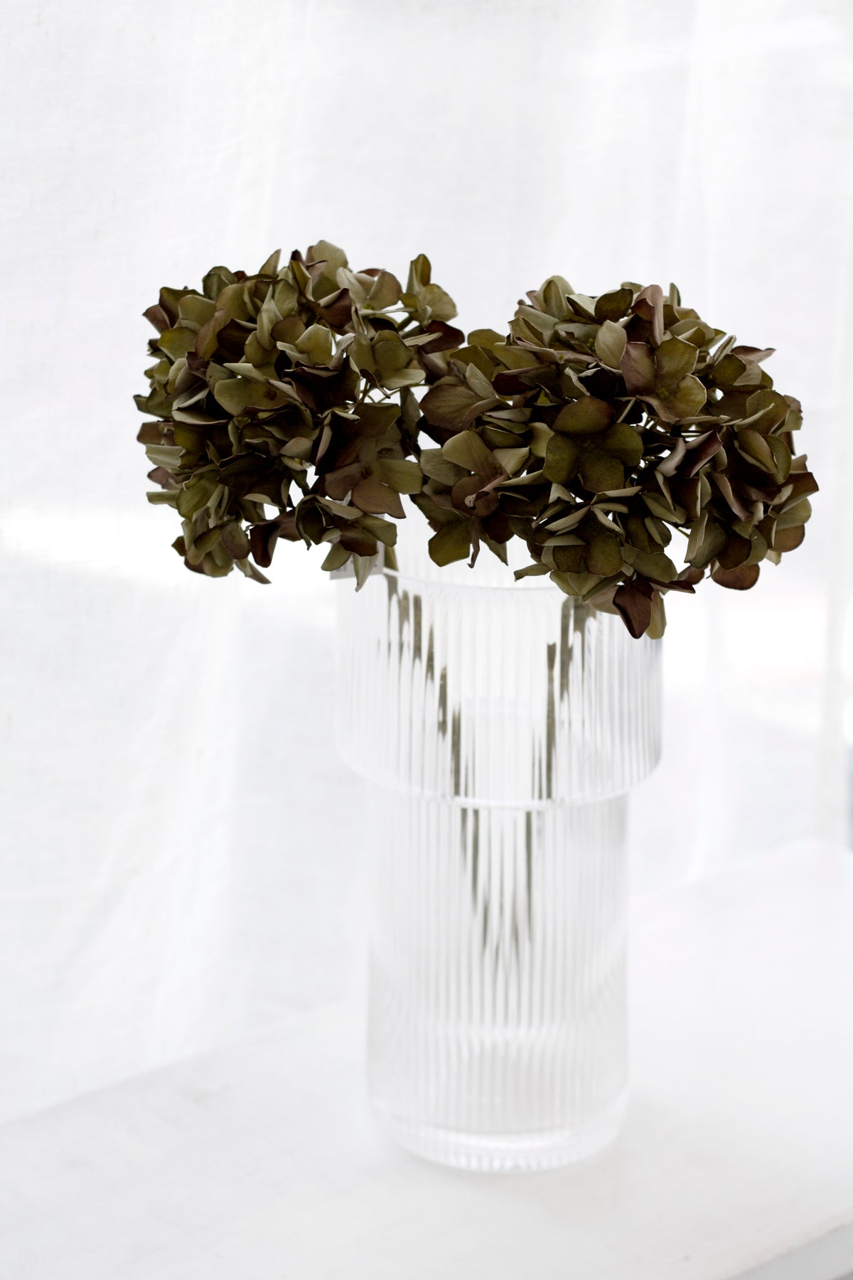 Two green faux hydrangea stems in a clear glass vase