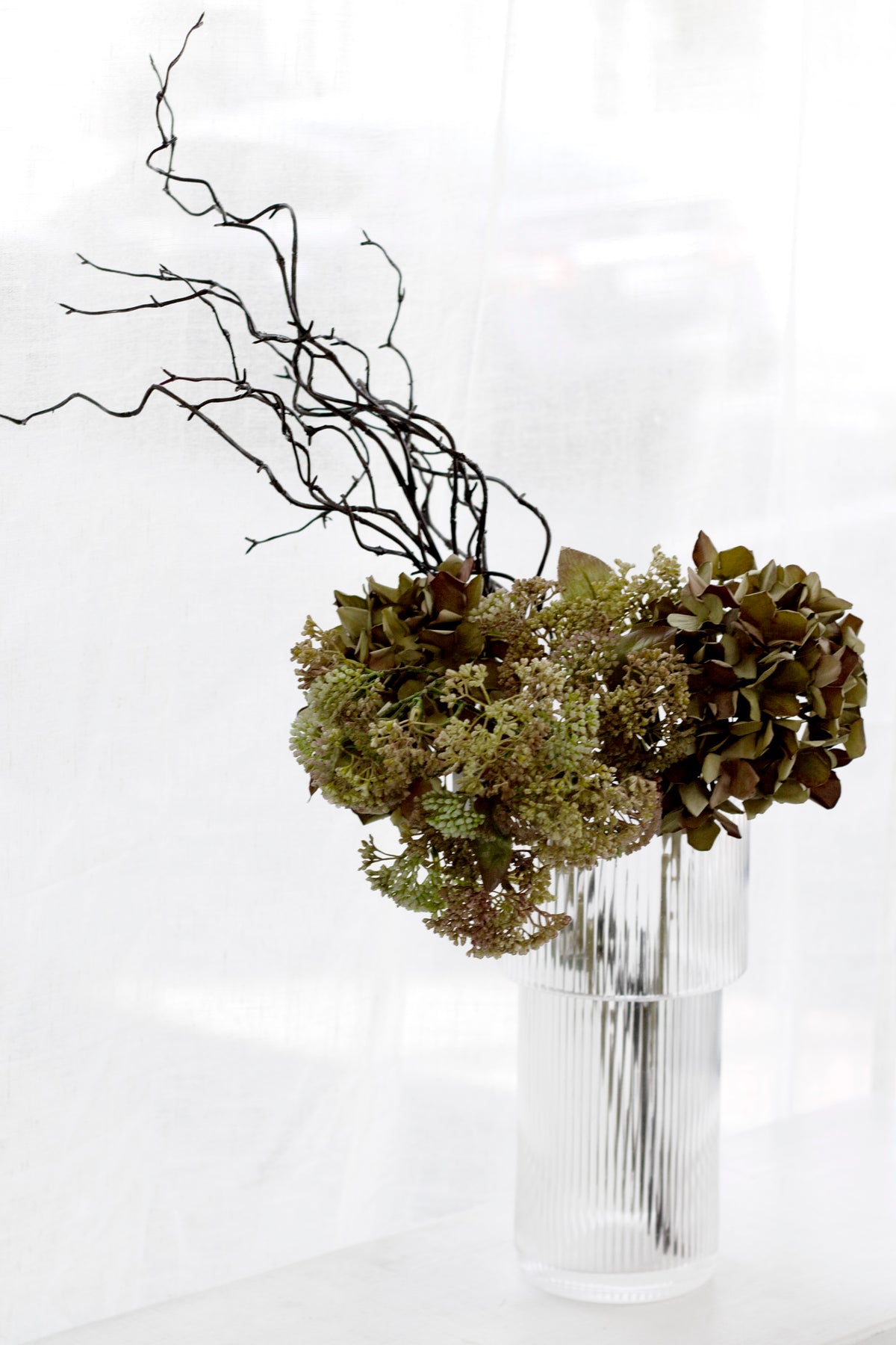 Green faux hydrangeas with dark twigs in a clear glass vase