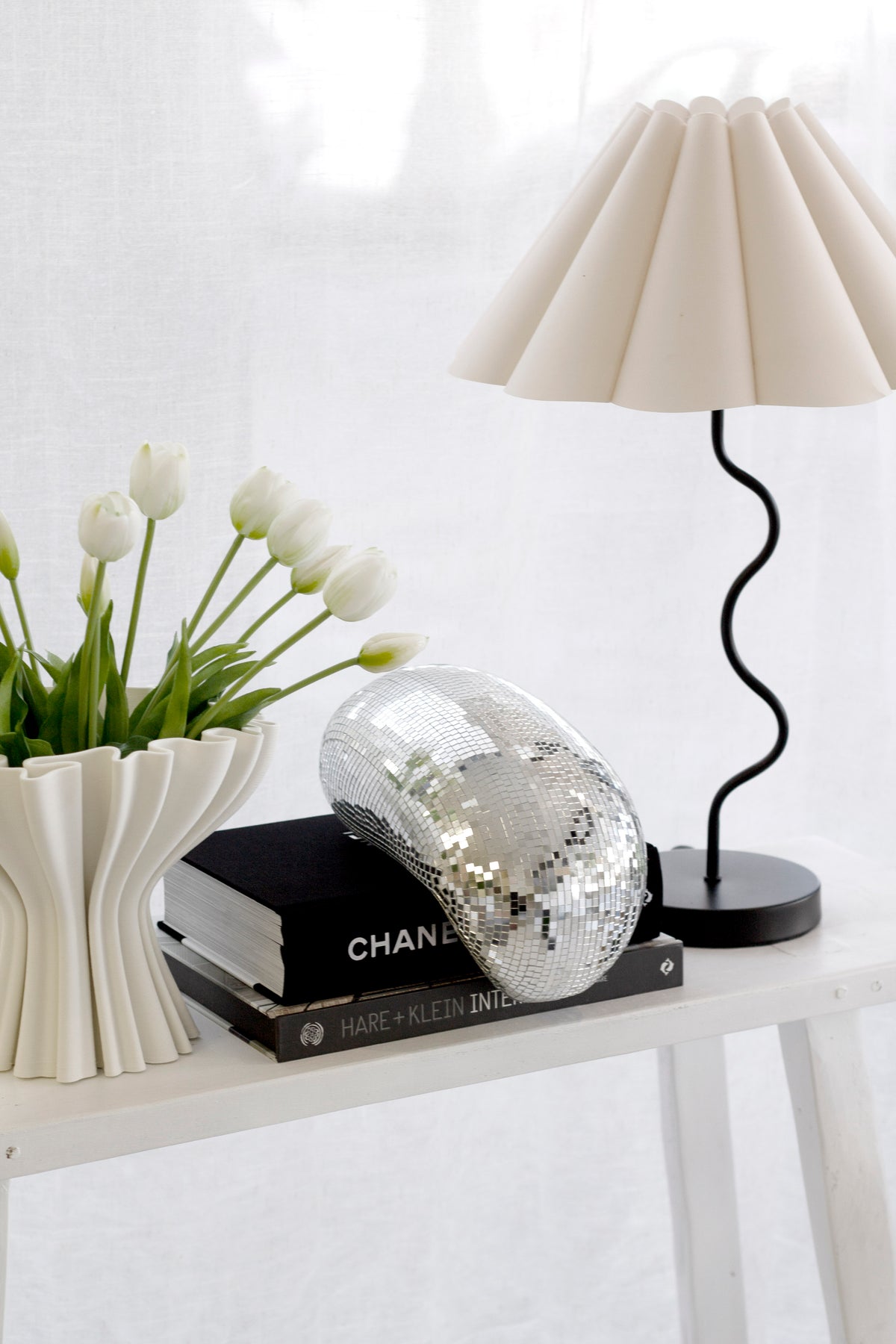 Melting disco ball on stacked books beside a pleated lamp and white tulips