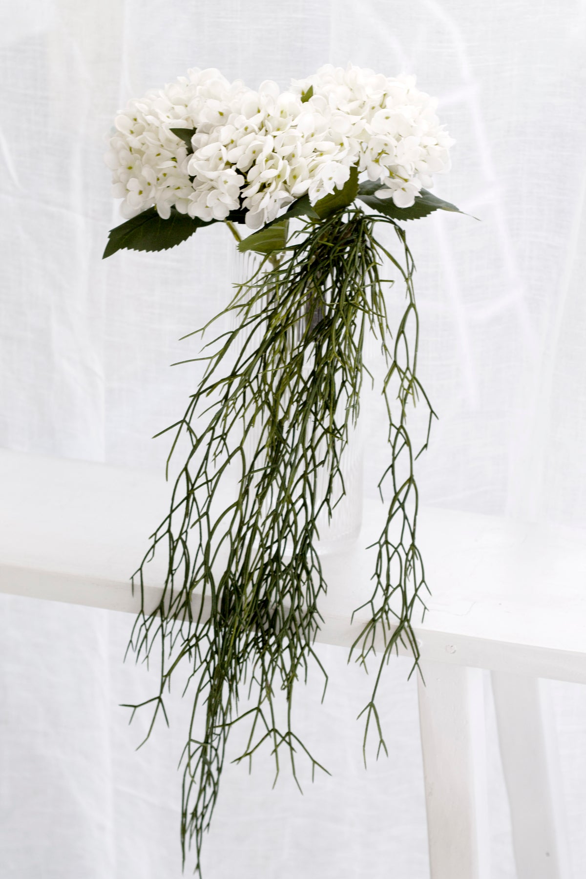 Faux rhipsalis with white orchids in a tall vase