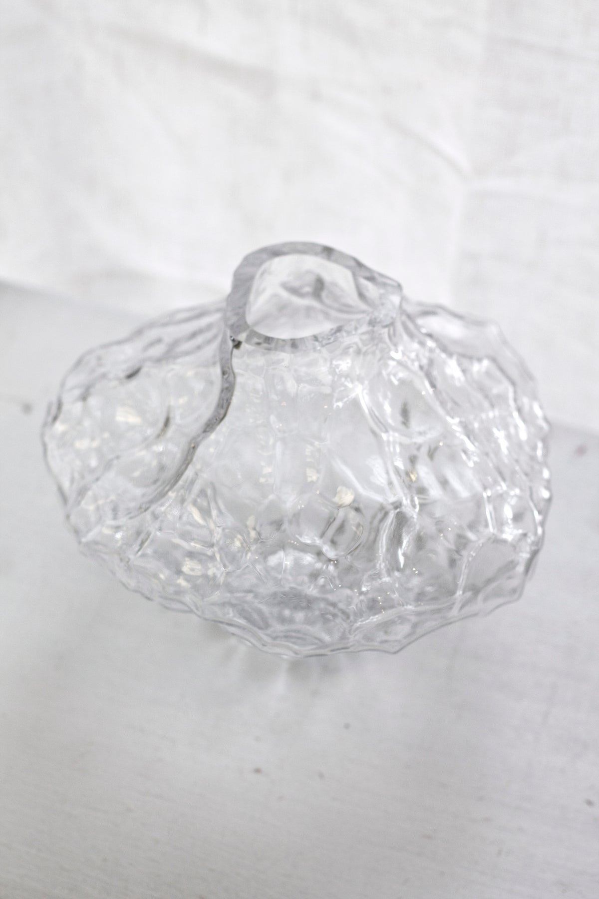 Clear rippled crystal glass vase seen from above on a pale surface against linen