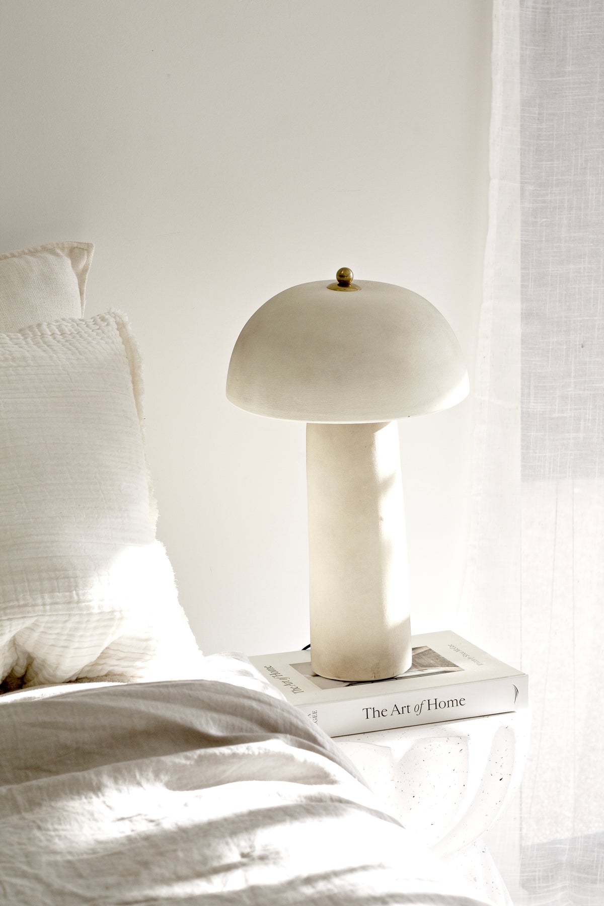 Xander lamp on a book on a bedside table beside white bedding