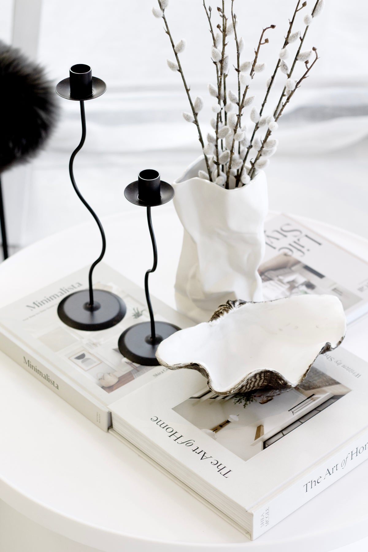 Black Hera pair on books beside a white crinkle vase of pussy willow and a clam shell