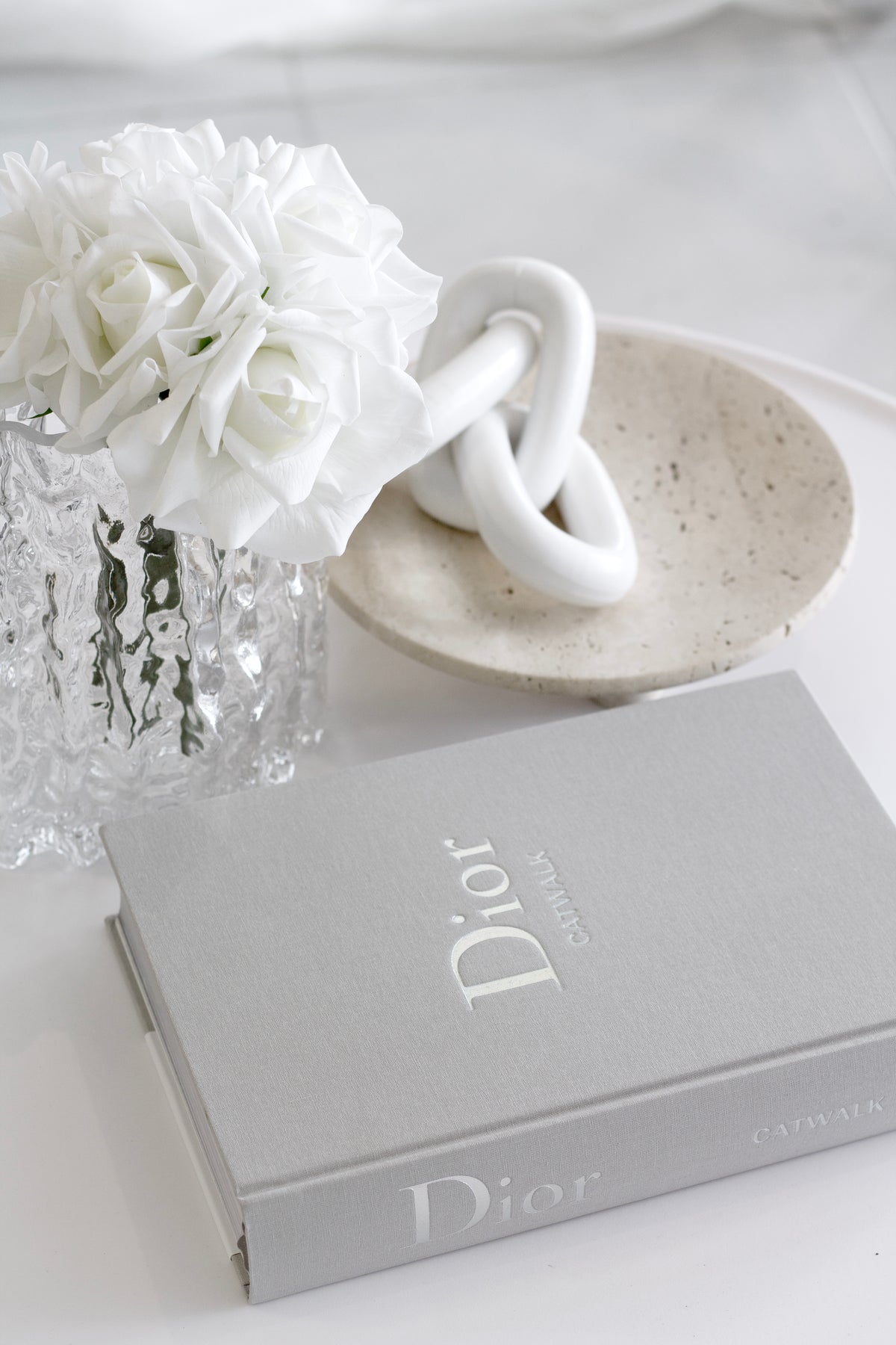 Nome stand with a white knot sculpture beside white hydrangeas on a grey coffee table book