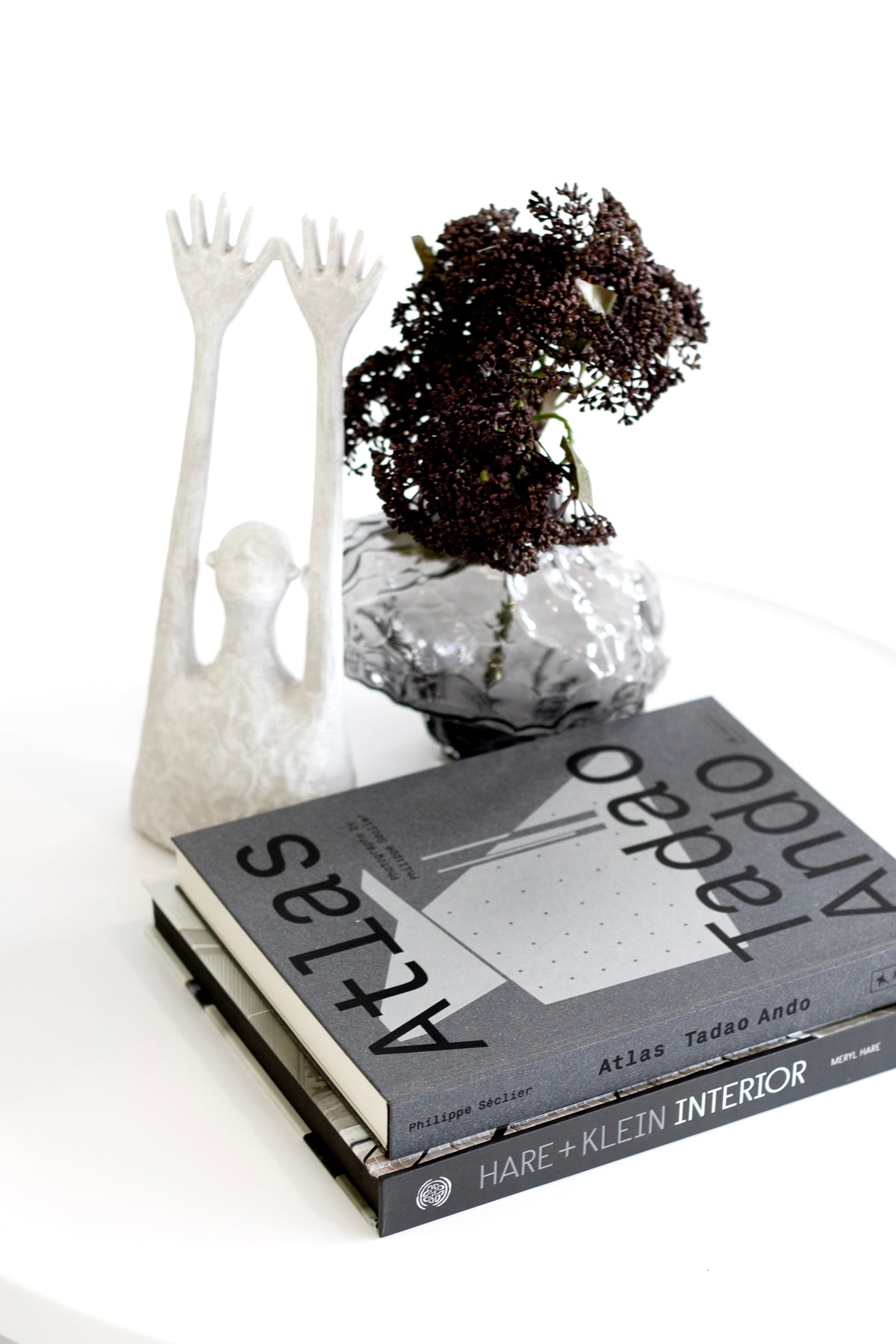 Clear rippled crystal glass vase with dark dried foliage on books beside a hand sculpture