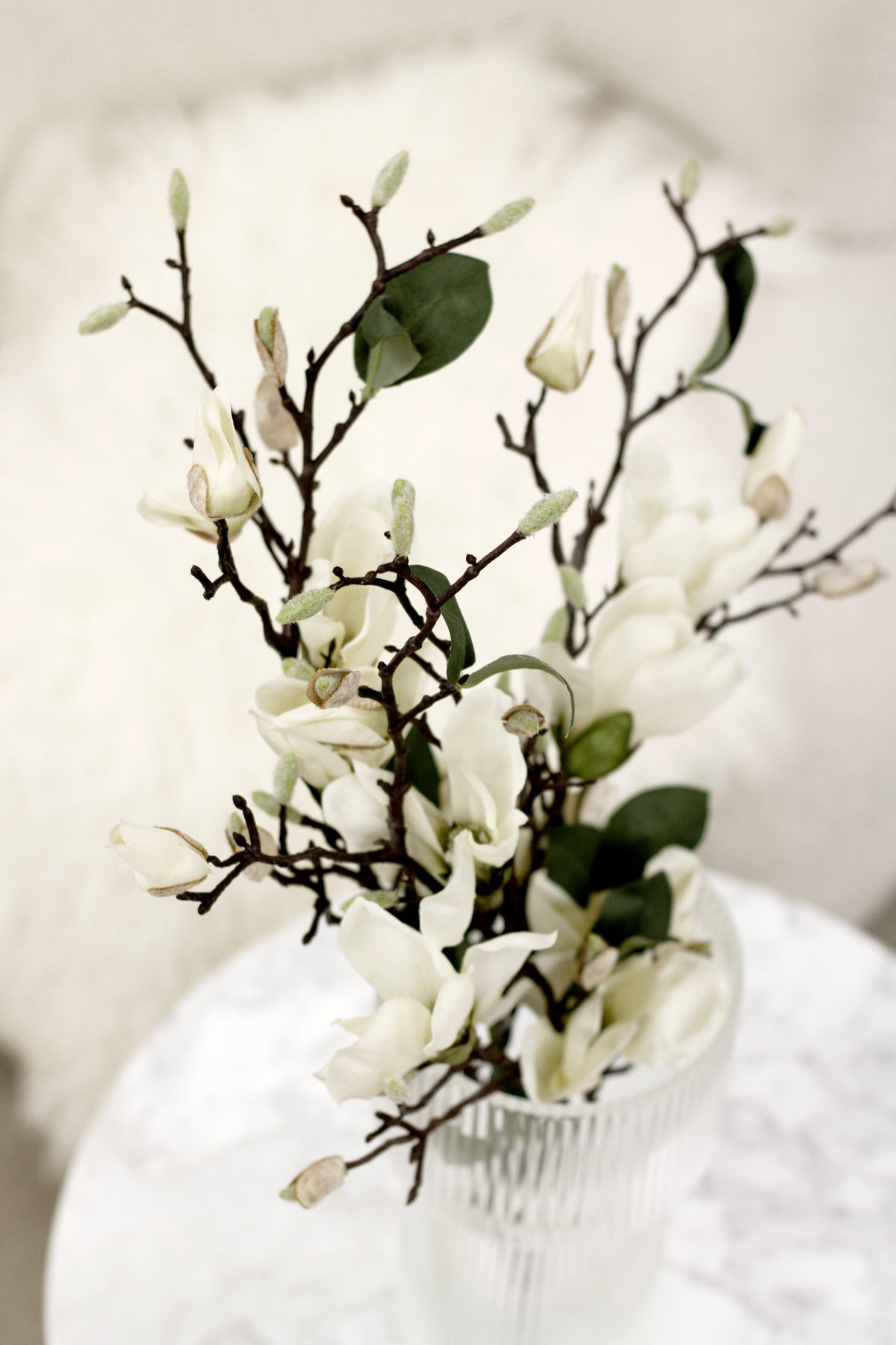 Faux white magnolia branches with dark stems in a clear ribbed glass vase