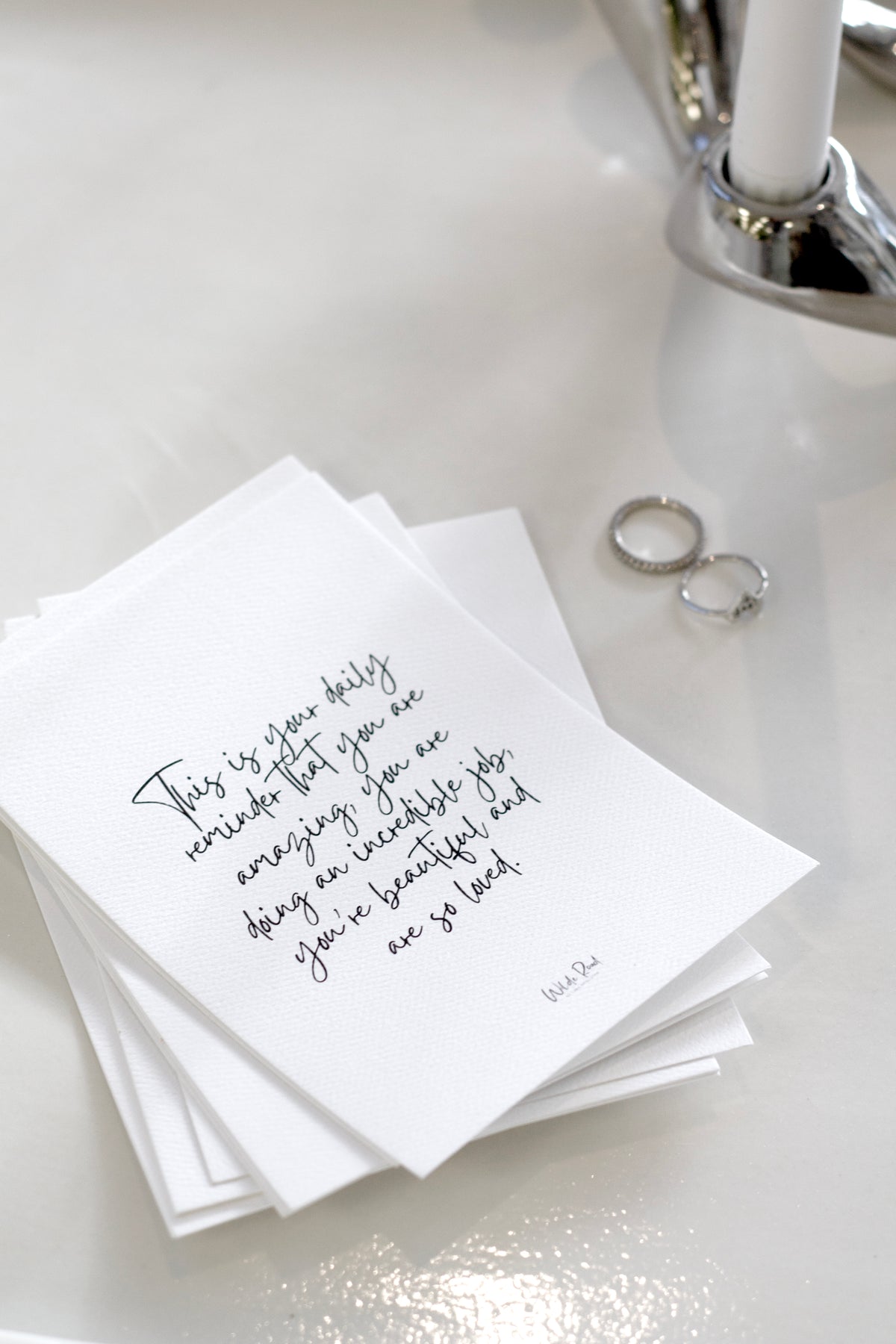 Affirmation cards fanned on a white surface beside a glass and rings
