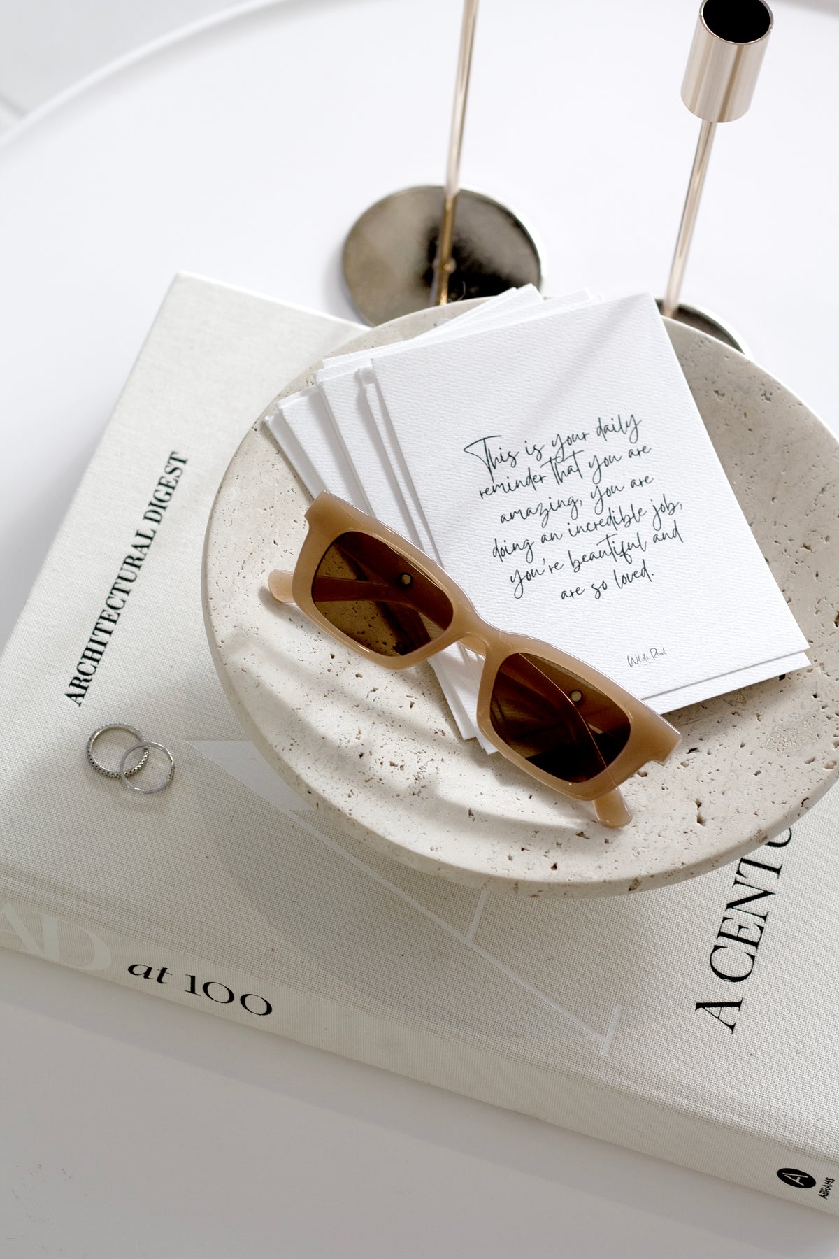 Nome stand holding handwritten cards and sunglasses on a coffee table book beside silver candlesticks