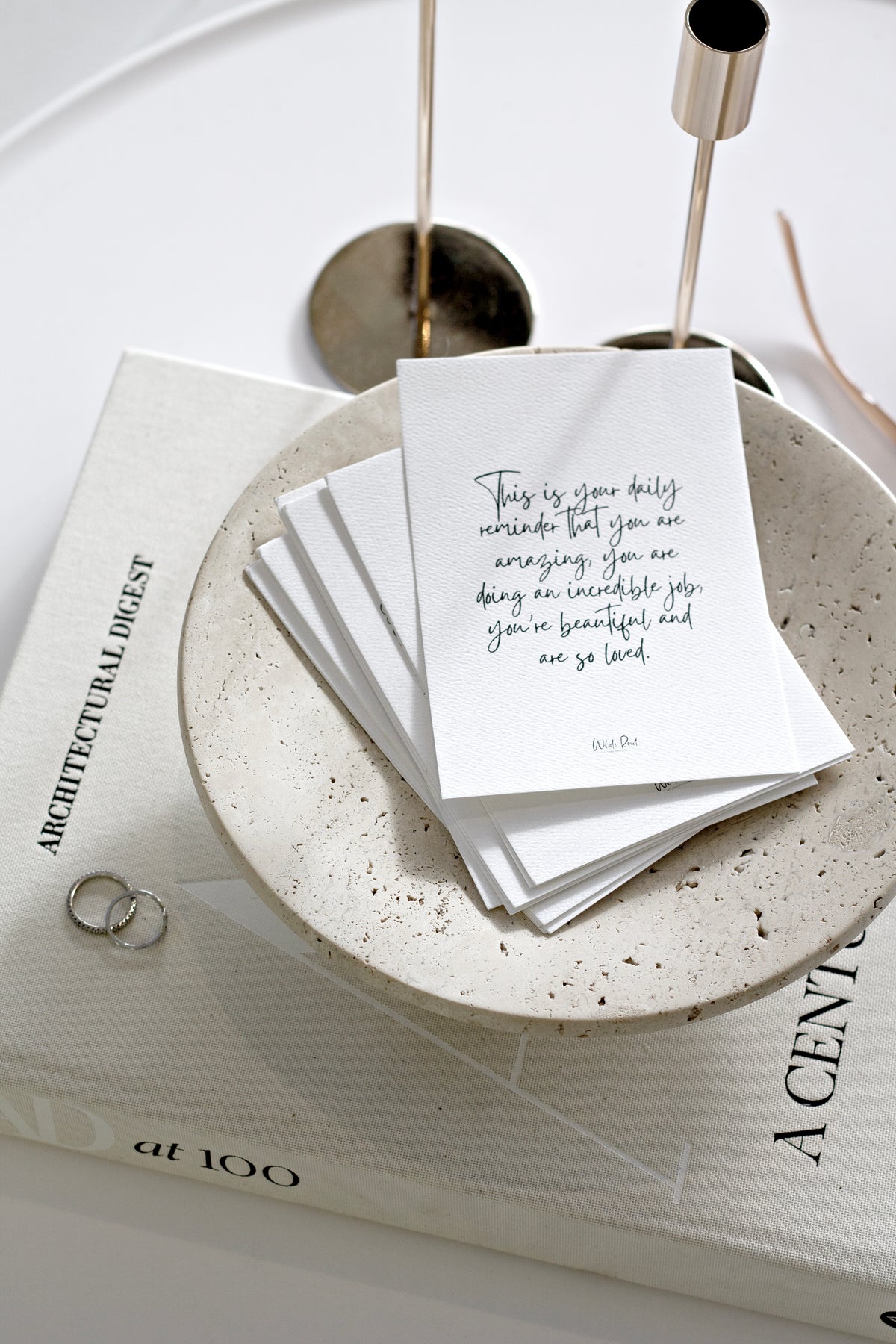 Nome travertine stand holding handwritten cards and gold rings on a coffee table book